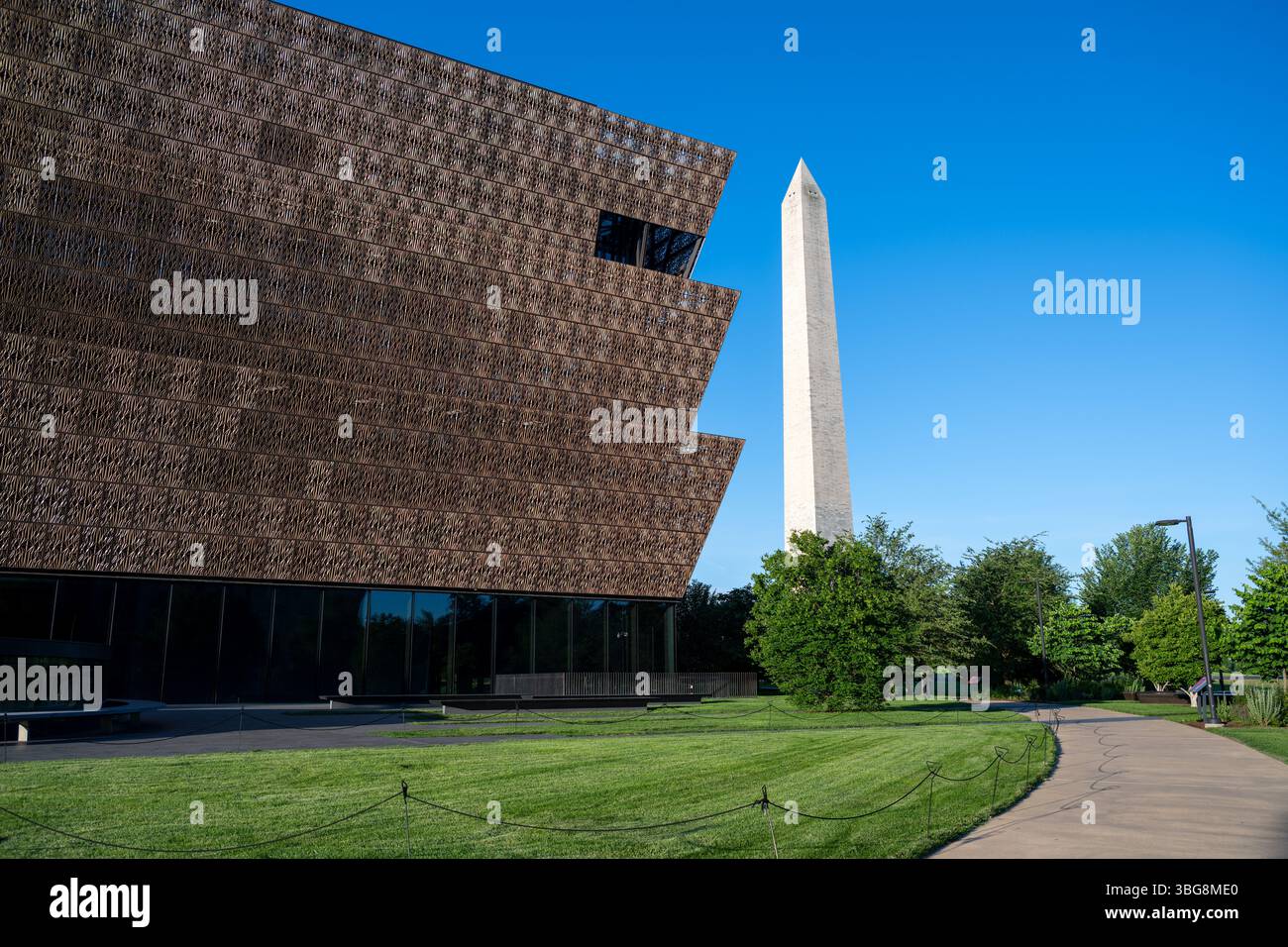 WASHINGTON DC - lo Smithsonian National Museum of African American History and Culture si erge in primo piano con il Washington Monument sullo sfondo del National Mall. Il caratteristico esterno in metallo color bronzo del museo, progettato dall'architetto David Adjaye e inaugurato nel settembre 2016, crea un contrasto sorprendente con l'obelisco in marmo bianco in onore del primo presidente americano. Questa vista cattura il dialogo architettonico tra il più recente museo Smithsonian della nazione e uno dei suoi monumenti più antichi. Foto Stock