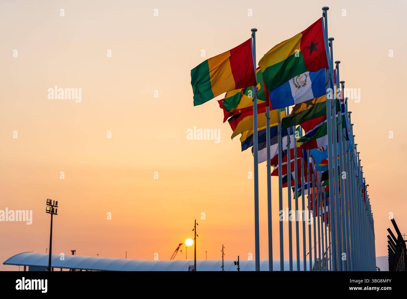 Le bandiere internazionali volano maestosamente contro un cielo limpido al crepuscolo all'ingresso dell'Expo 2025 Osaka Kansai durante il tramonto. Osaka, Giappone Foto Stock