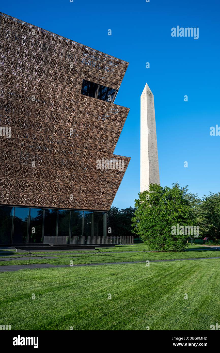 WASHINGTON DC - lo Smithsonian National Museum of African American History and Culture si erge in primo piano con il Washington Monument sullo sfondo del National Mall. Il caratteristico esterno in metallo color bronzo del museo, progettato dall'architetto David Adjaye e inaugurato nel settembre 2016, crea un contrasto sorprendente con l'obelisco in marmo bianco in onore del primo presidente americano. Questa vista cattura il dialogo architettonico tra il più recente museo Smithsonian della nazione e uno dei suoi monumenti più antichi. Foto Stock