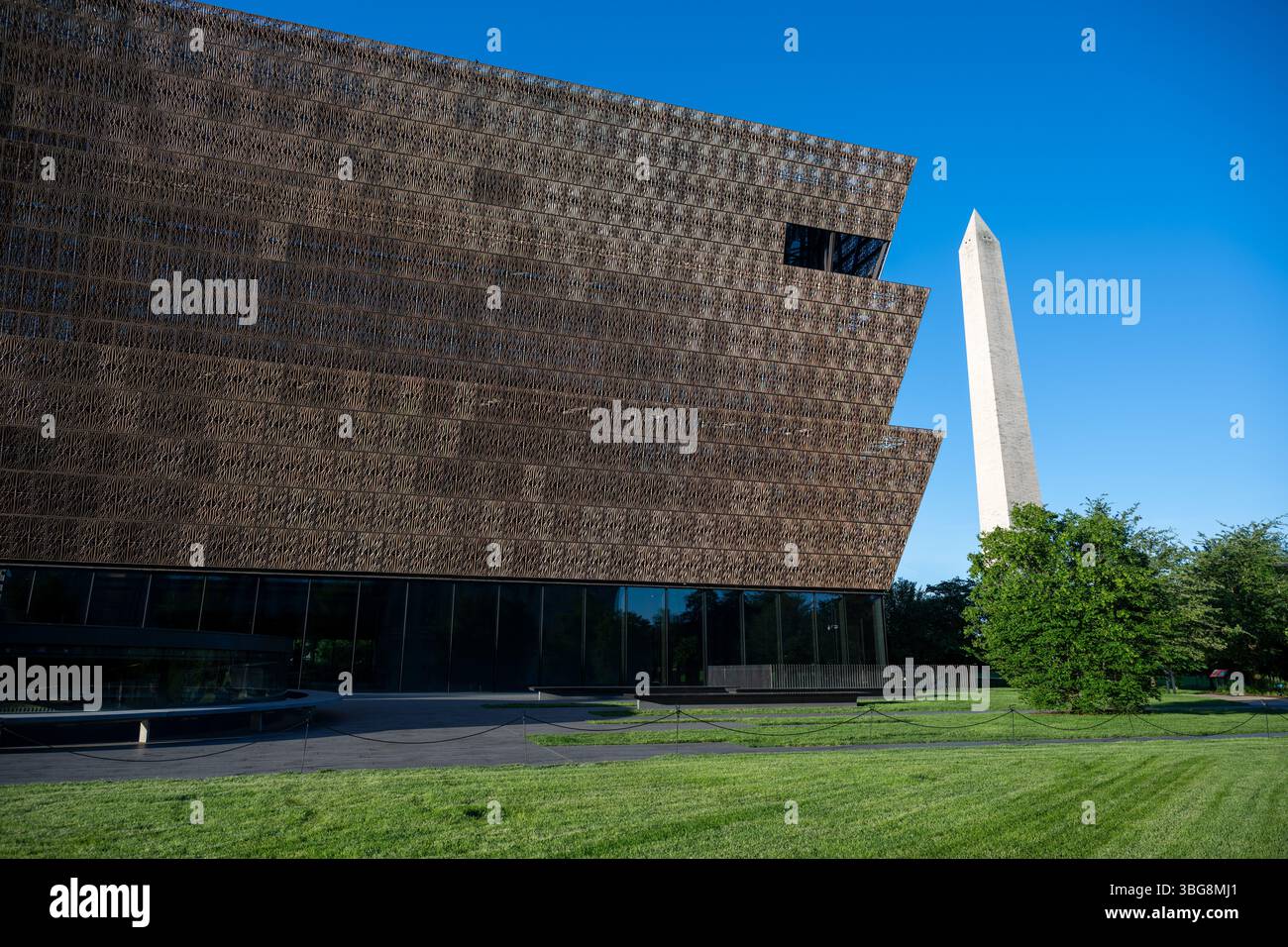 WASHINGTON DC - lo Smithsonian National Museum of African American History and Culture si erge in primo piano con il Washington Monument sullo sfondo del National Mall. Il caratteristico esterno in metallo color bronzo del museo, progettato dall'architetto David Adjaye e inaugurato nel settembre 2016, crea un contrasto sorprendente con l'obelisco in marmo bianco in onore del primo presidente americano. Questa vista cattura il dialogo architettonico tra il più recente museo Smithsonian della nazione e uno dei suoi monumenti più antichi. Foto Stock