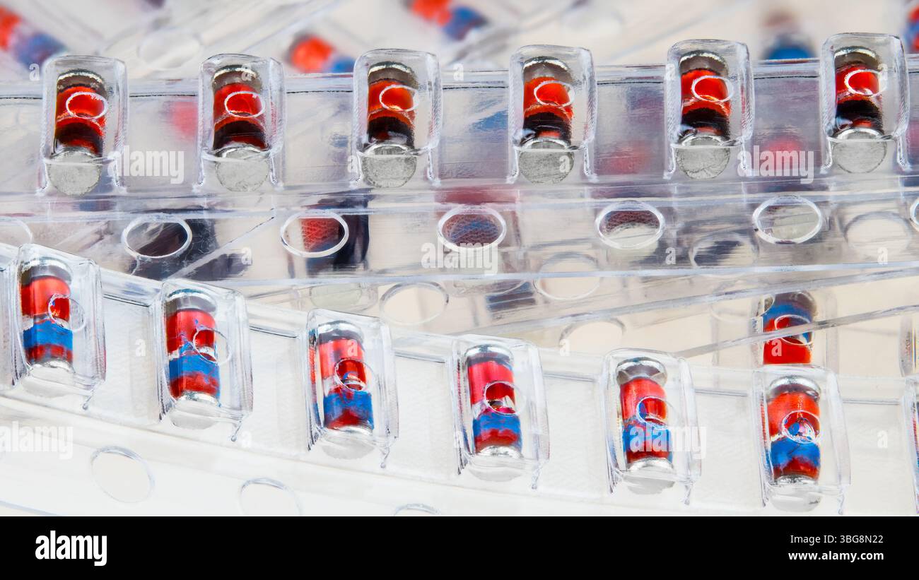 Primo piano dei diodi Zener SMD confezionati in strisce blister in plastica su sfondo bianco. Pile di componenti elettronici rossi in imballaggi trasparenti. Foto Stock
