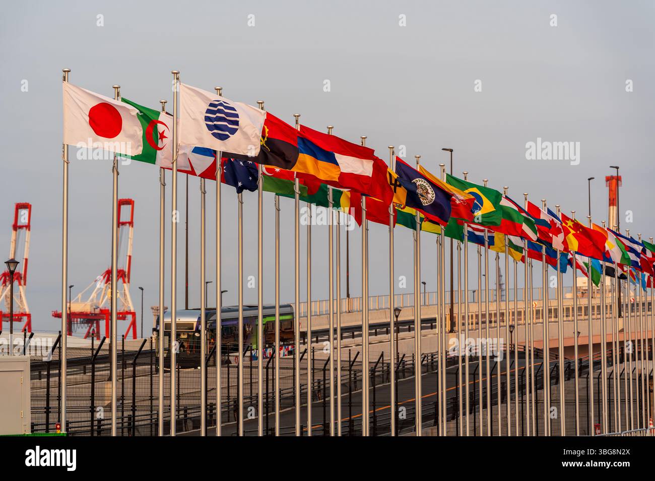 Le bandiere internazionali volano maestosamente contro un cielo limpido al crepuscolo all'ingresso dell'Expo 2025 Osaka Kansai durante il tramonto. Osaka, Giappone Foto Stock