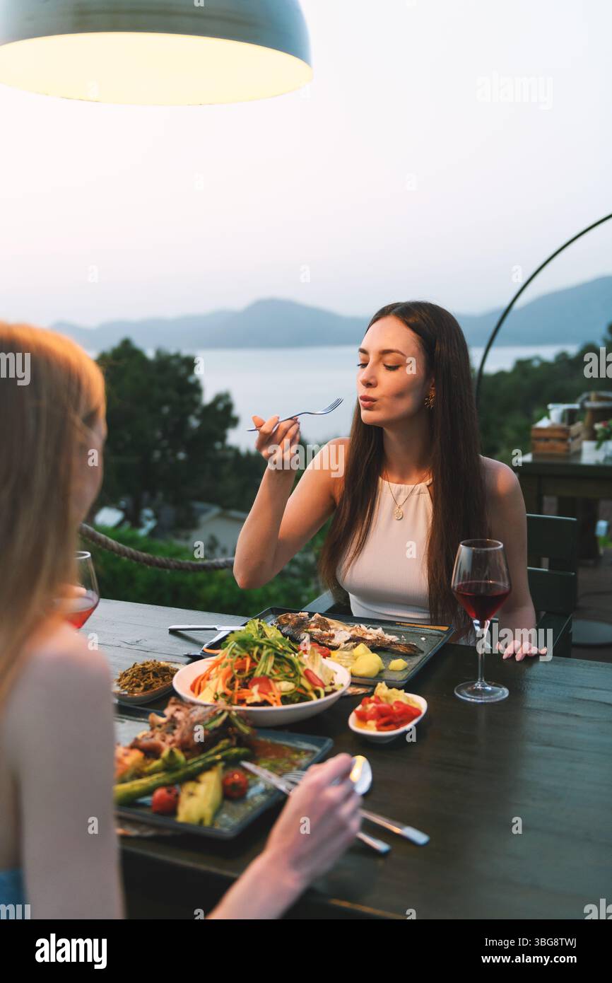 Una bruna anni '20 gusta il suo pasto serale e il suo vino nell'ambiente elegante di un lussuoso ristorante dell'hotel. Foto Stock