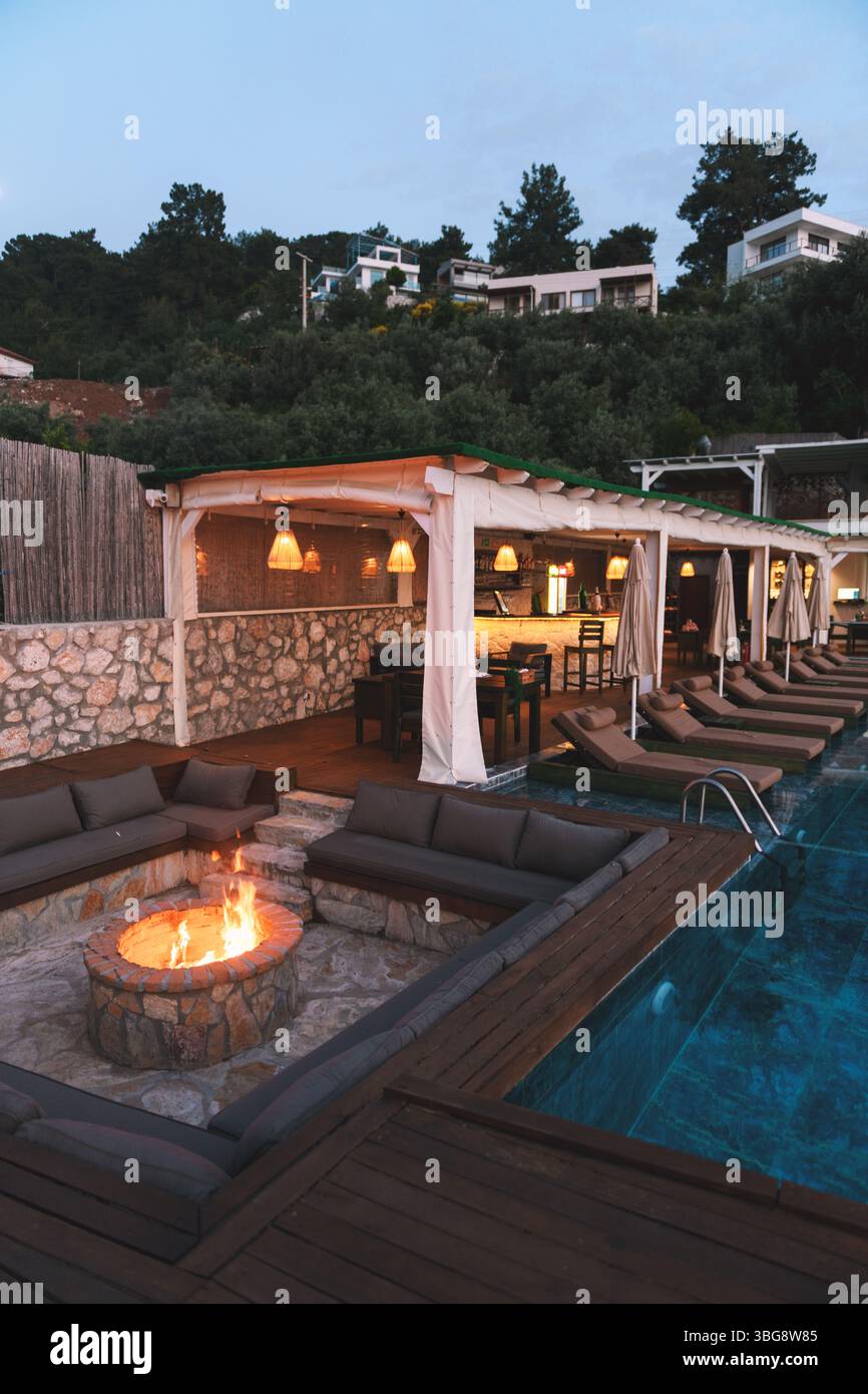 Un accogliente caminetto brucia in un hotel di lusso con il bar e la piscina visibili sullo sfondo durante le ore serali. Foto Stock