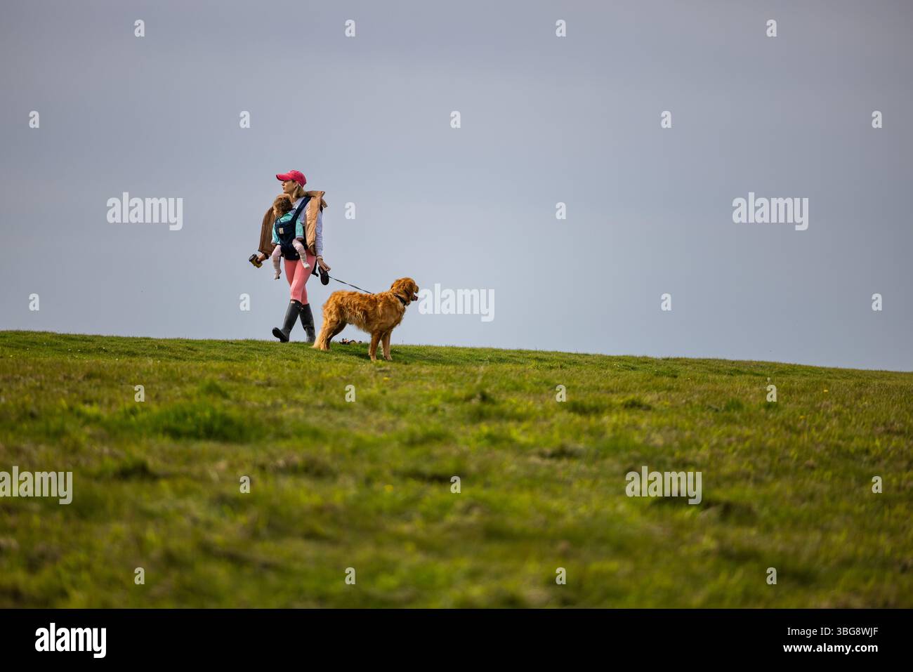 Mamma che cammina con il bambino in un portabagagli aperto sulle colline sotto il cielo grigio, scenario di vita rurale, ambiente rurale del Regno Unito. Foto Stock