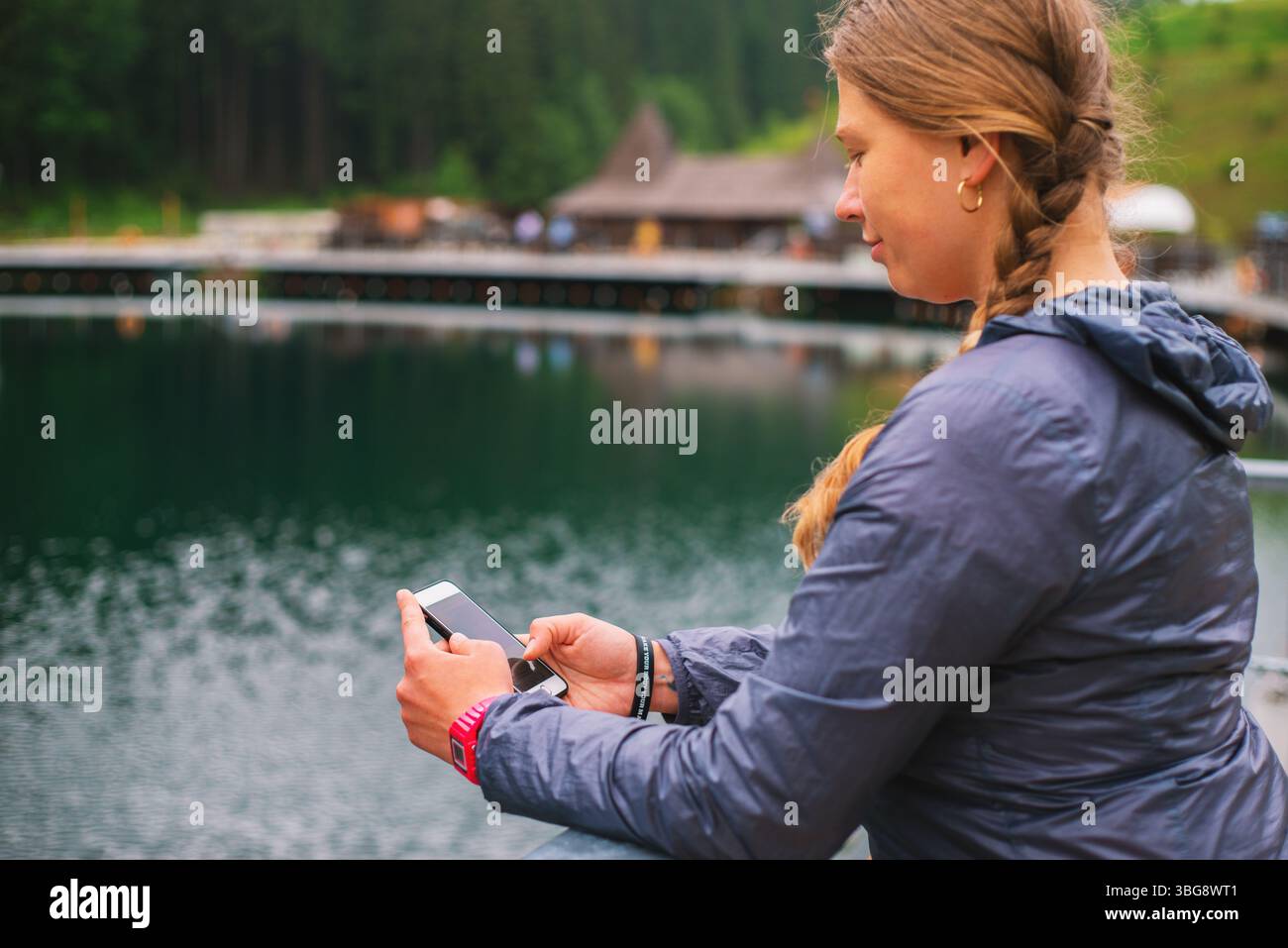 Giovane turista con i capelli intrecciati che usa lo smartphone all'aperto in una località sciistica sulle montagne Foto Stock