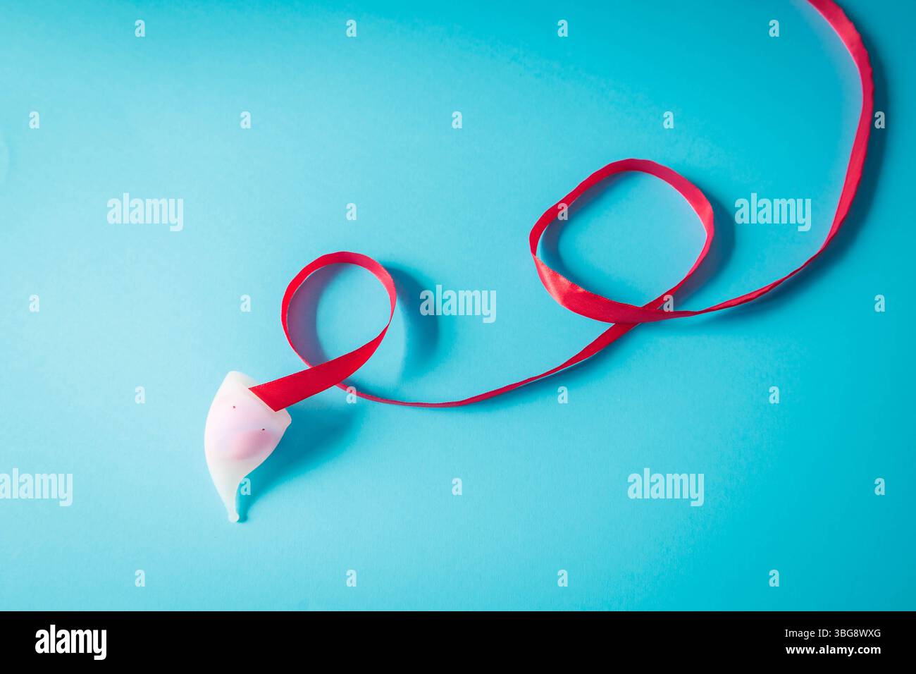 Composizione minimalista di una coppetta mestruale bianca con nastro rosso che scorre su sfondo blu. Immagine simbolica che promuove l'igiene femminile e l'ecocoscienza Foto Stock