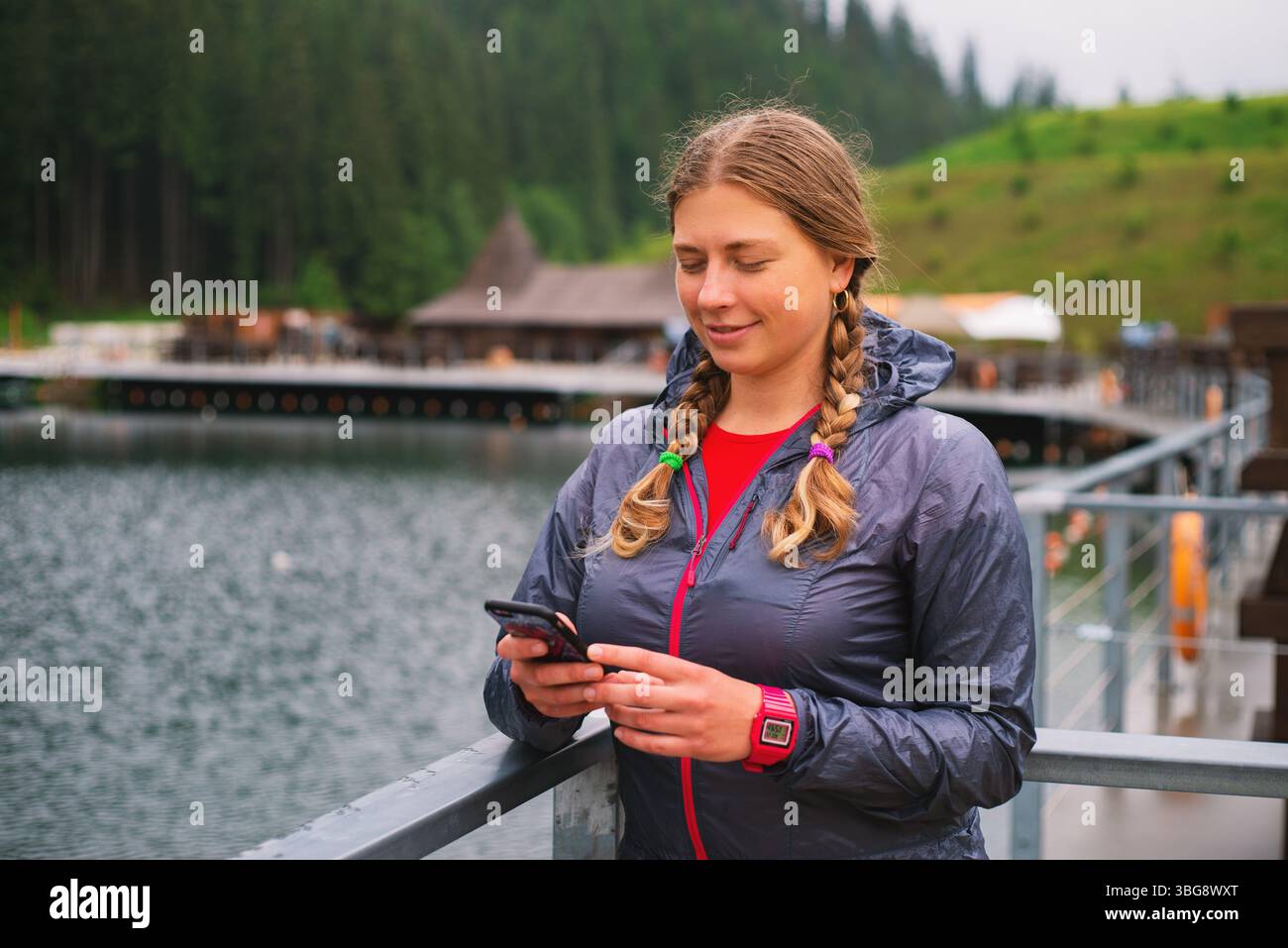 Giovane turista con i capelli intrecciati che usa lo smartphone all'aperto in una località sciistica sulle montagne Foto Stock