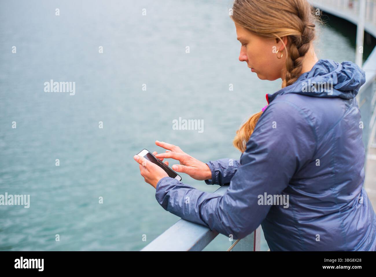 Giovane turista con i capelli intrecciati che usa lo smartphone all'aperto in una località sciistica sulle montagne Foto Stock