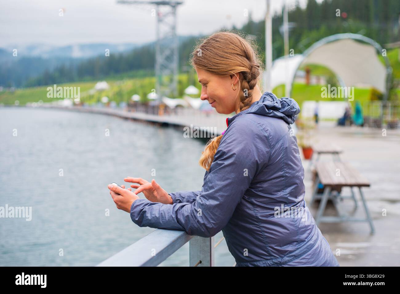 Giovane turista con i capelli intrecciati che usa lo smartphone all'aperto in una località sciistica sulle montagne Foto Stock