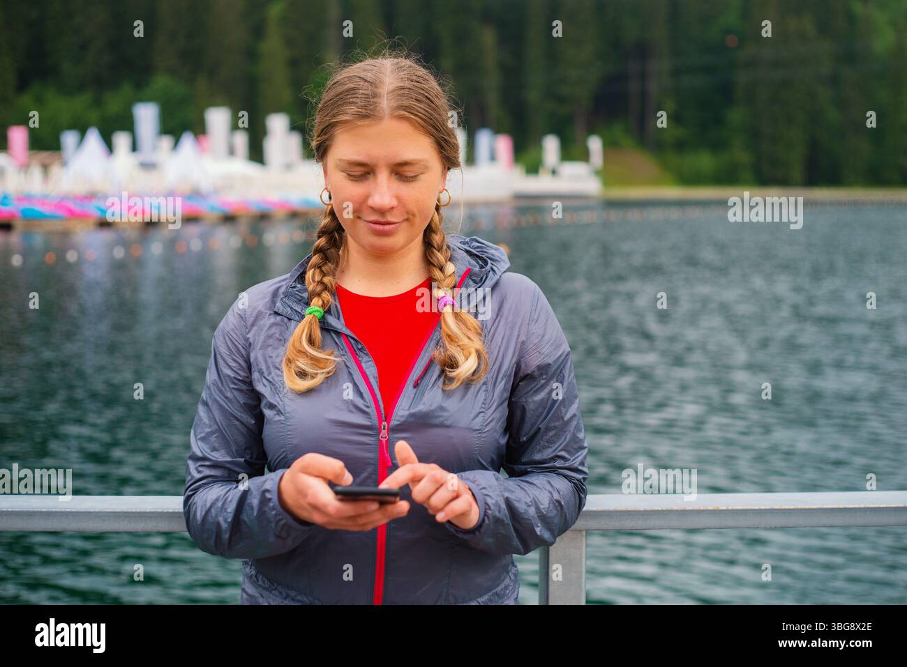 Giovane turista con i capelli intrecciati che usa lo smartphone all'aperto in una località sciistica sulle montagne Foto Stock