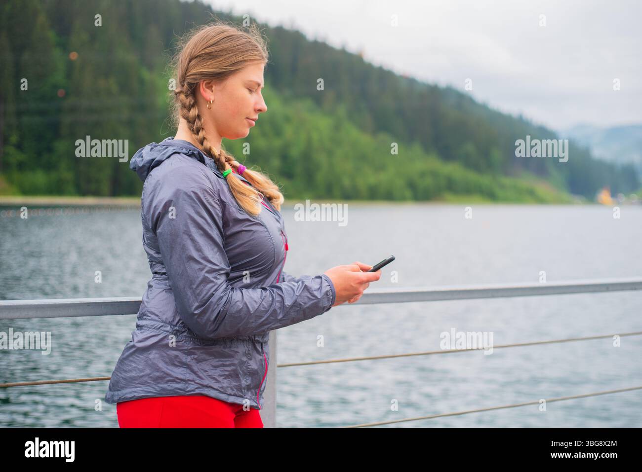 Giovane turista con i capelli intrecciati che usa lo smartphone all'aperto in una località sciistica sulle montagne Foto Stock
