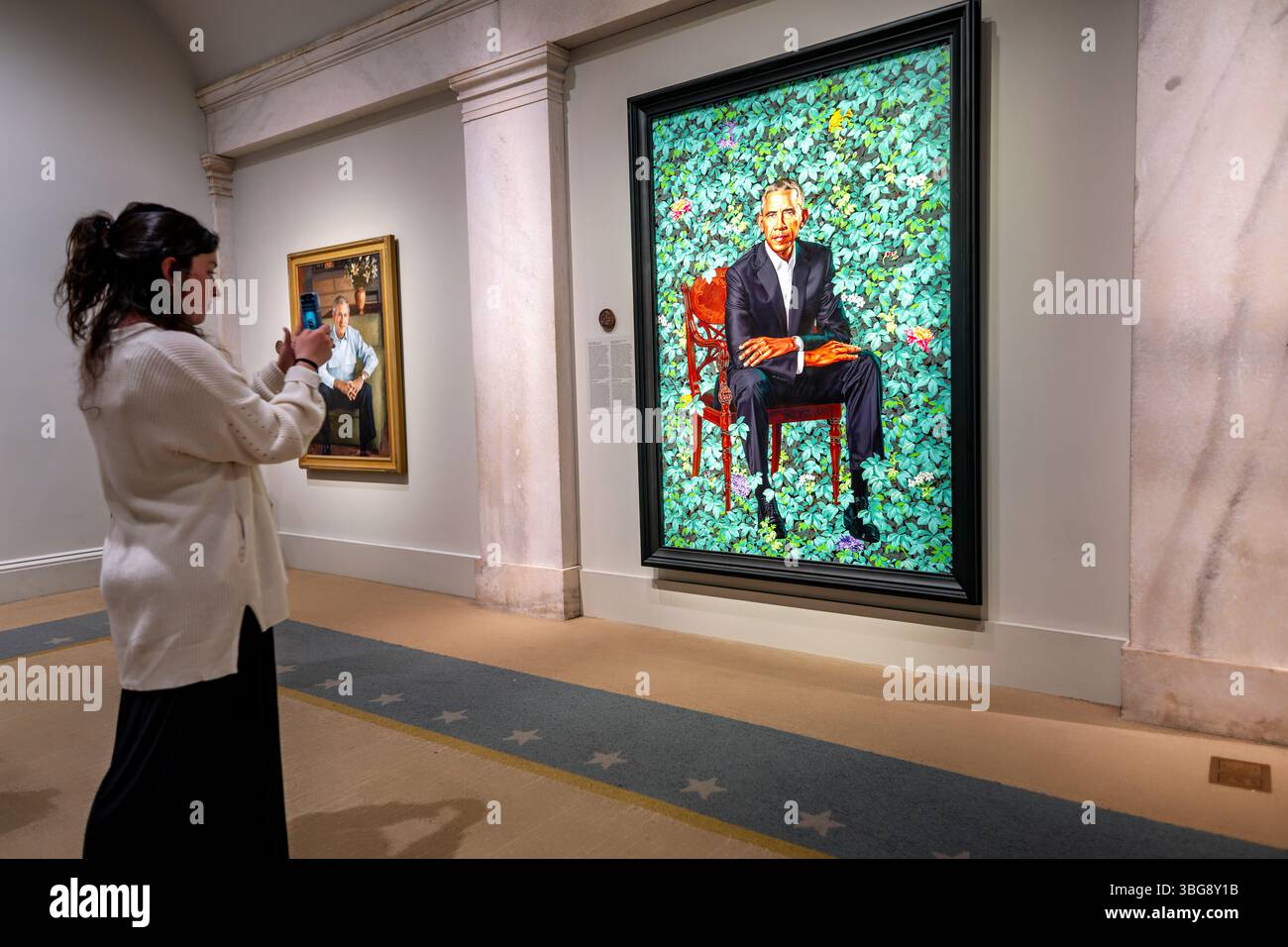 Barack Obama Ritratto di Kehinde Wiley nella National Portrait Gallery di Washington DC | WASHINGTON D.C., Stati Uniti - Un visitatore del museo cattura il ritratto di Barack Obama di Kehinde Wiley del 2018 su uno smartphone alla National Portrait Gallery, con un ritratto di George W. Bush visibile sul muro adiacente. La collezione presidenziale della galleria, l'unico set completo al di fuori della Casa Bianca, è ospitata nell'Old Patent Office Building, un punto di riferimento del revival greco completato in fasi tra il 1836 e il 1867. Foto Stock