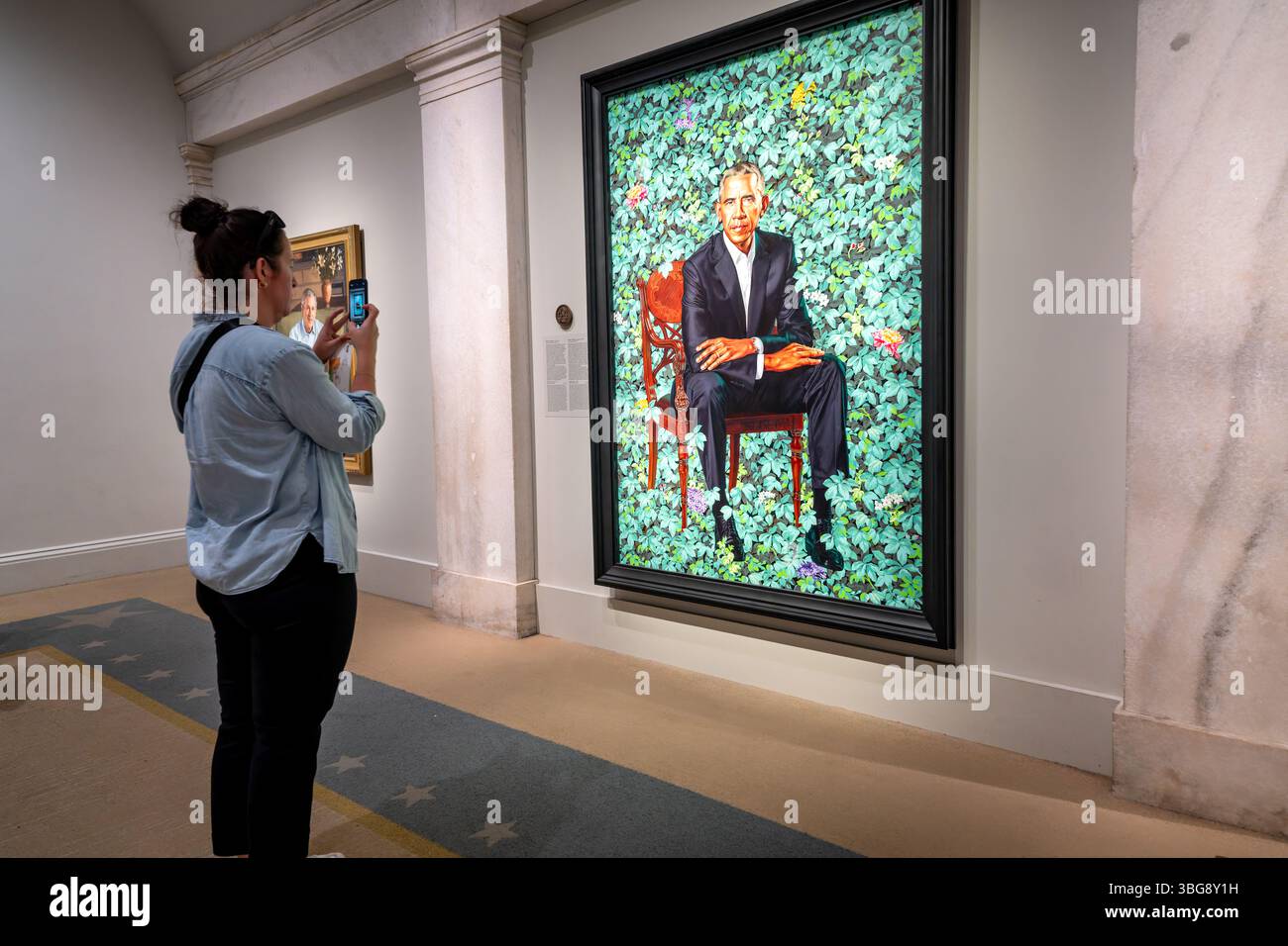 WASHINGTON DC - Un visitatore scatta una fotografia del ritratto presidenziale ufficiale di Barack Obama alla Smithsonian National Portrait Gallery. Il ritratto, dipinto da Kehinde Wiley nel 2018, raffigura il 44° presidente seduto su uno sfondo di verde fogliame con fiori. L'opera fa parte della collezione permanente del museo di ritratti presidenziali, che include dipinti ufficiali di ogni presidente degli Stati Uniti. La National Portrait Gallery, situata nello storico edificio dell'Ufficio brevetti, ospita l'unica collezione completa di ritratti presidenziali della nazione fuori dalla Casa Bianca. Foto Stock