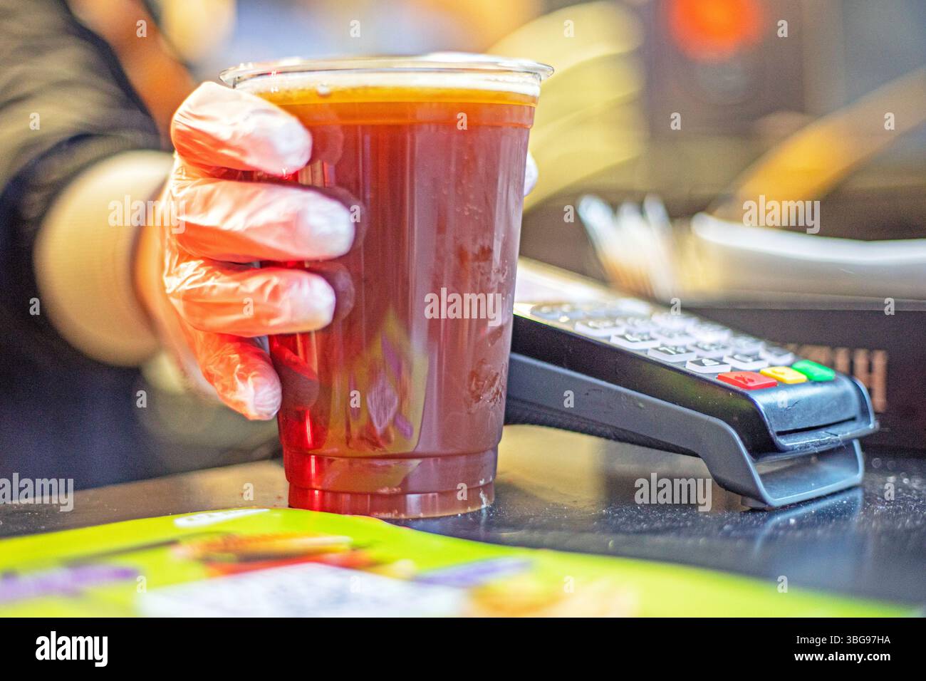 vendere in un bicchiere di plastica trasparente monouso di materiali riciclabili birra fresca da bere o kvass con guanti. cibo di strada Foto Stock