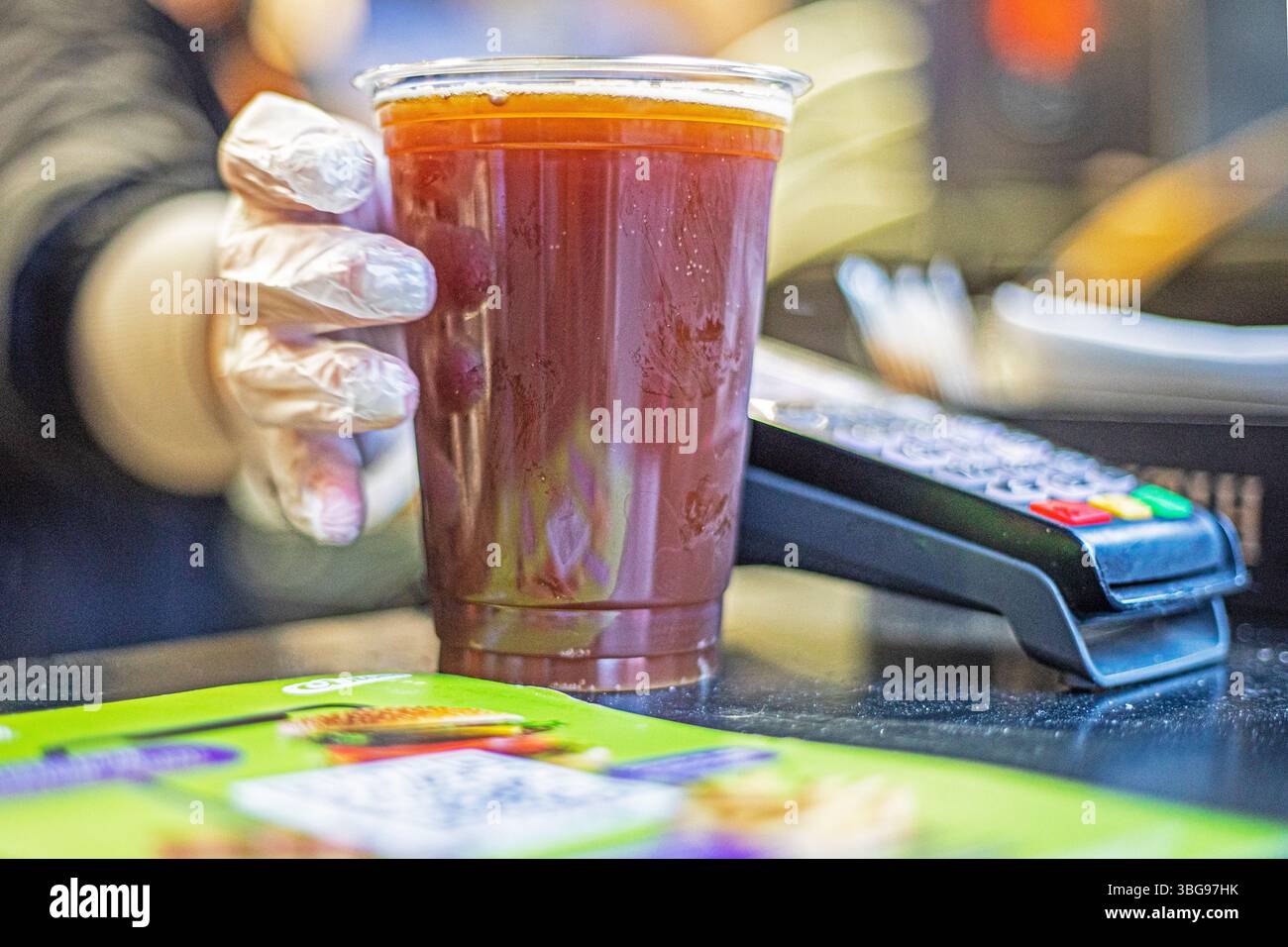 vendere in un bicchiere di plastica trasparente monouso di materiali riciclabili birra fresca da bere o kvass con guanti. cibo di strada Foto Stock
