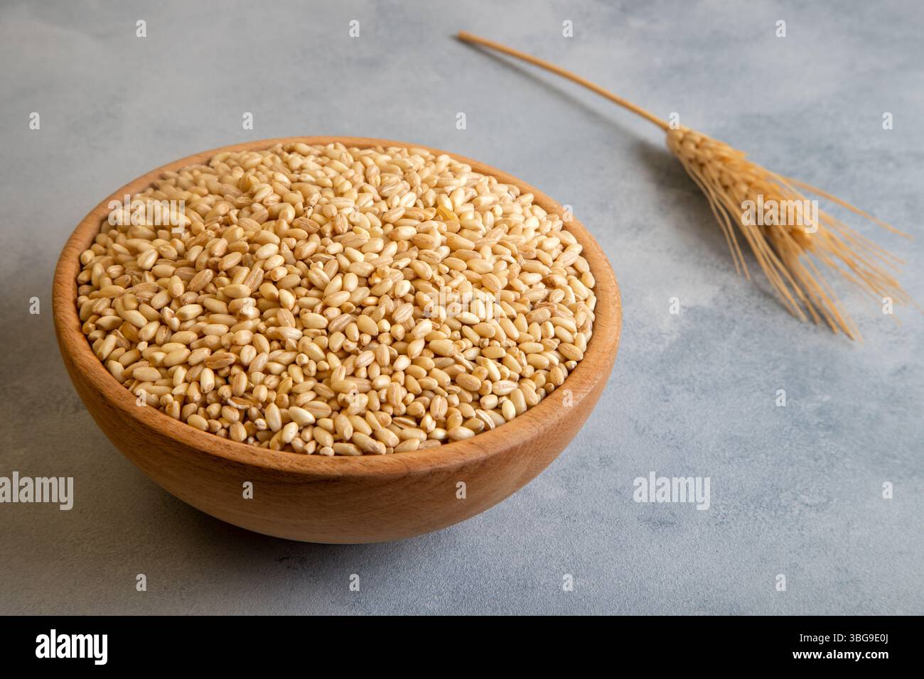 Grani di grano in una ciotola di legno e orecchie su sfondo luminoso, vista dall'alto Foto Stock