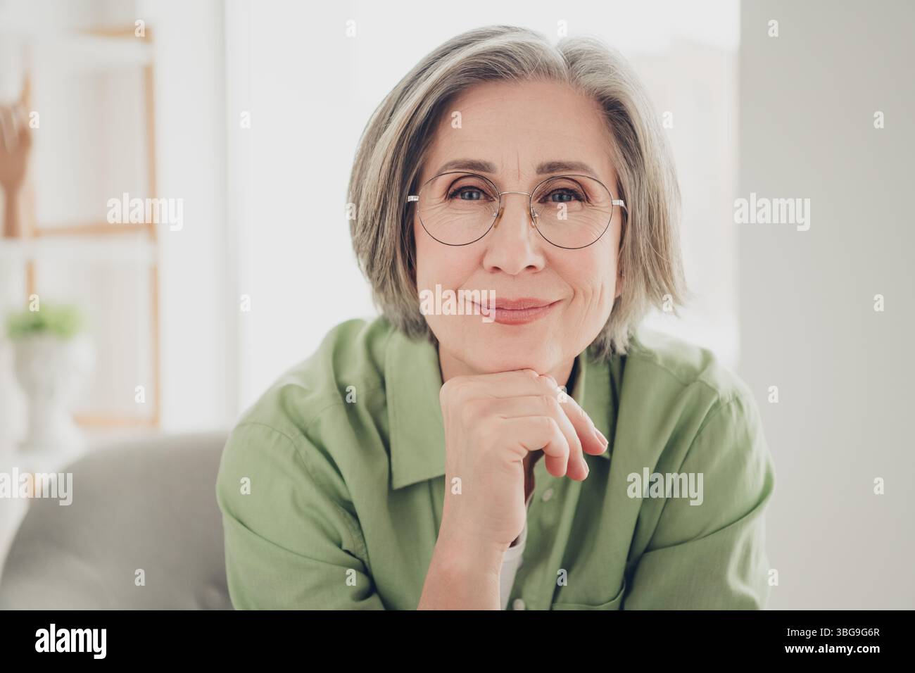 Affascinante donna matura con capelli grigi che indossa gli occhiali da vista seduti comodamente in casa e che proietta sicurezza e felicità Foto Stock