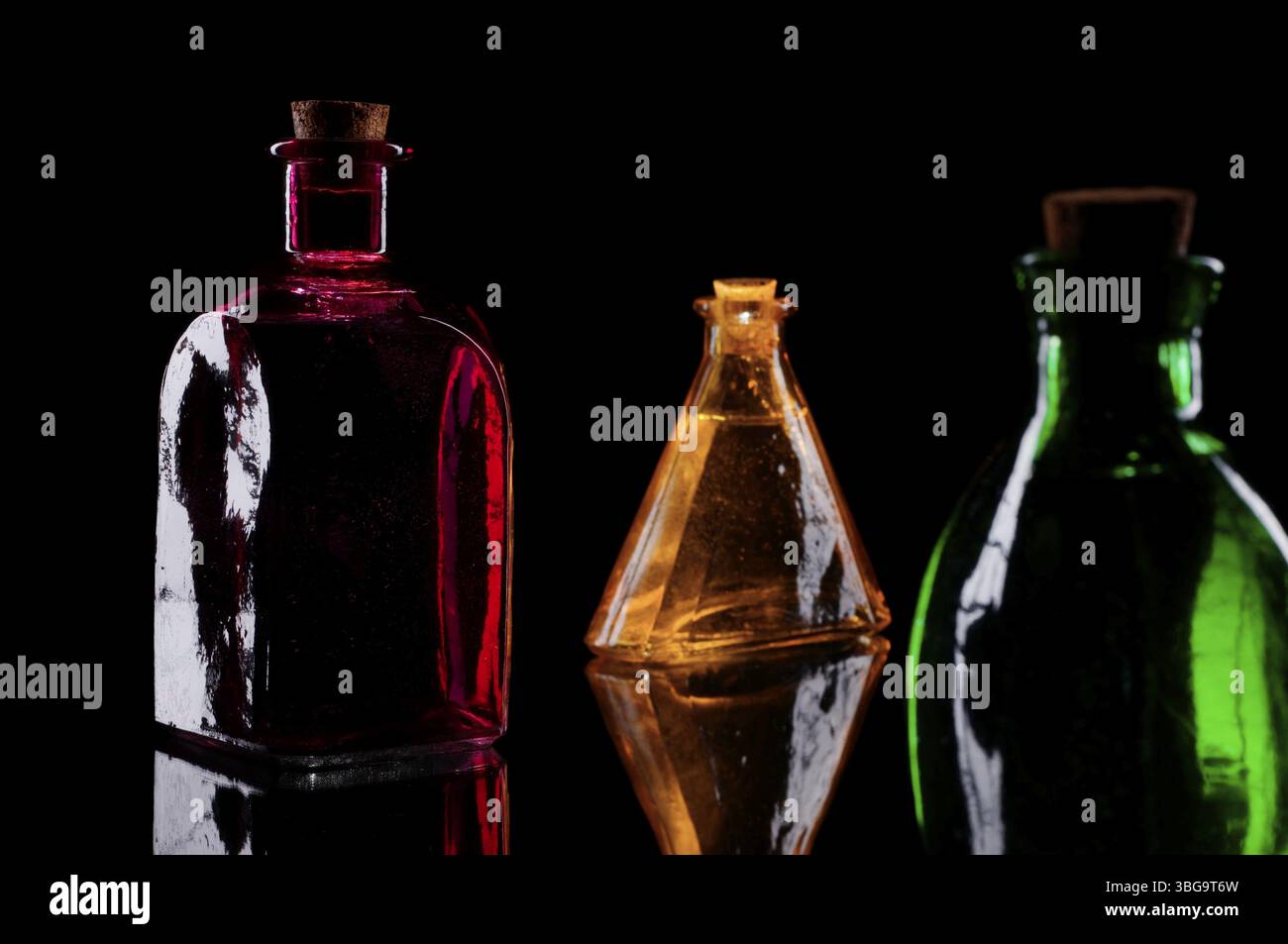STILL Life di tre bottiglie decorative colorate con tappi in sughero su vetro su sfondo nero Foto Stock