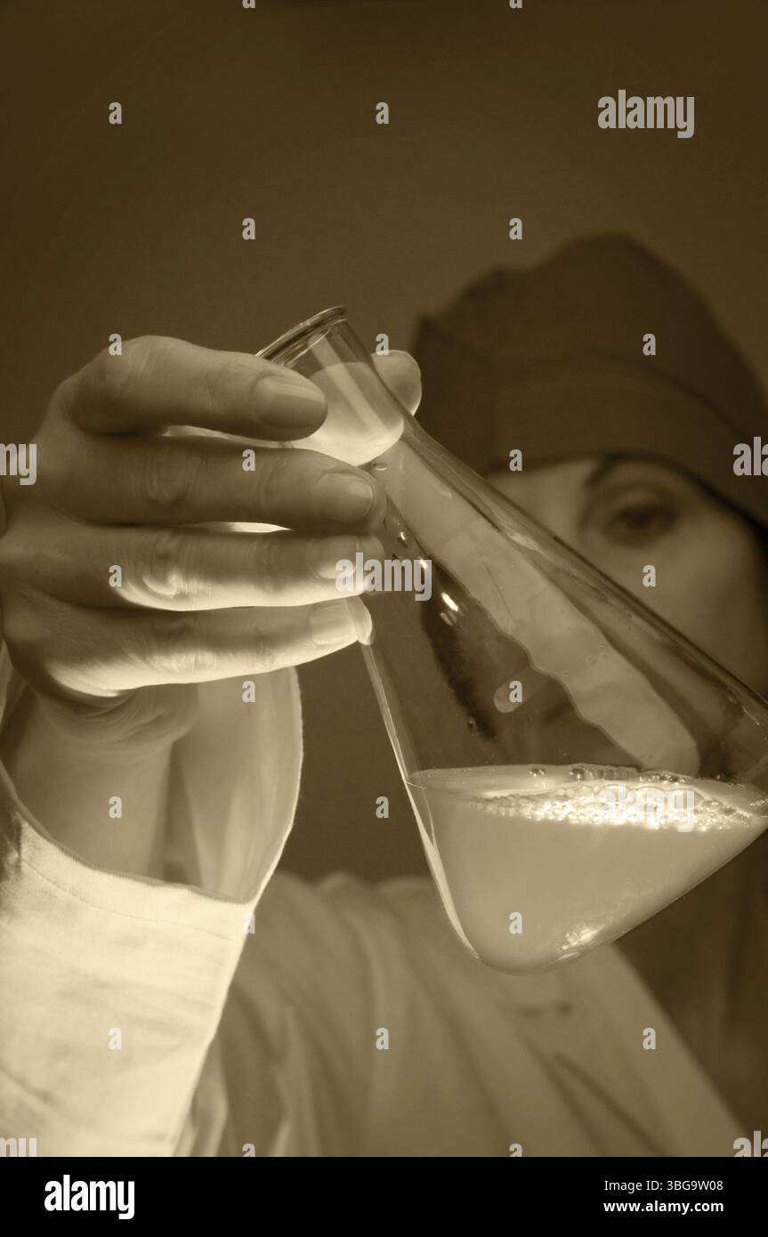 Foto testa e spalle di una donna di mezza età con un cappotto bianco e copricapo che sventola una fiasca di Erlenmeyer verso la fotocamera, tonificante seppia Foto Stock