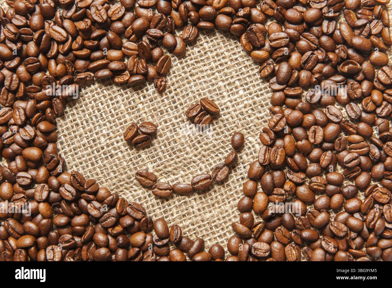Vista che riempie il formato di una cornice inclinata a forma di cuore composta da chicchi di caffè tostati con un sorriso su un sacco Foto Stock