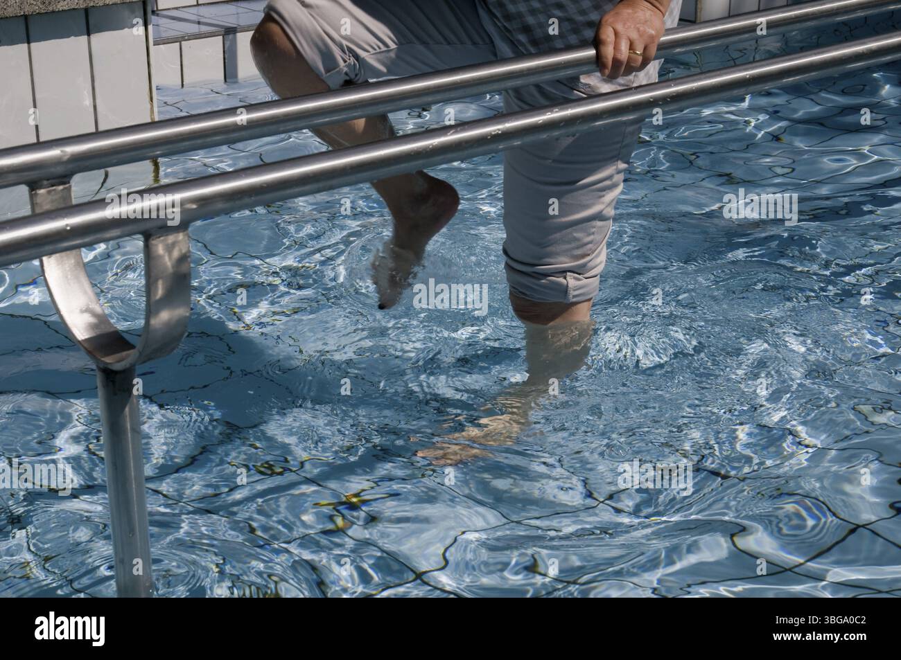 Foto esterna di gambe femminili che camminano in acqua (cura Kneipp) in una piscina piastrellata con corrimano in acciaio inox Foto Stock
