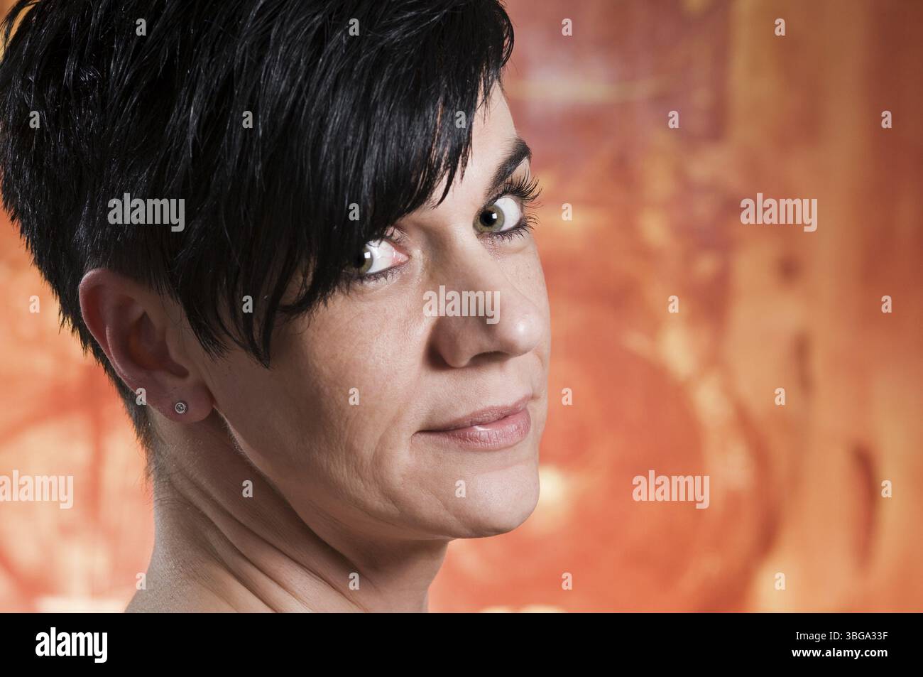 Ritratto della testa laterale di una donna di mezza età dai capelli neri su uno sfondo arancione e guardando verso la fotocamera Foto Stock