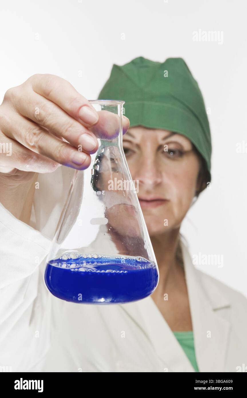 L'assistente di laboratorio tiene una lampadina di vetro con un liquido blu e un aspetto di controllo Foto Stock