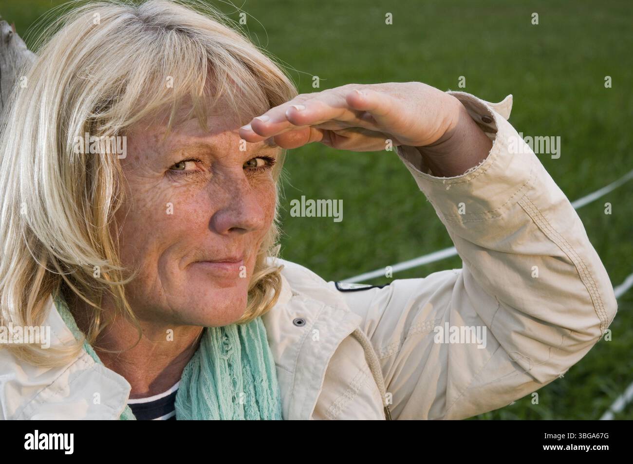 Ritratto della testa laterale di una donna bionda di mezza età di fronte a un prato verde che sembra amichevole nella fotocamera Foto Stock