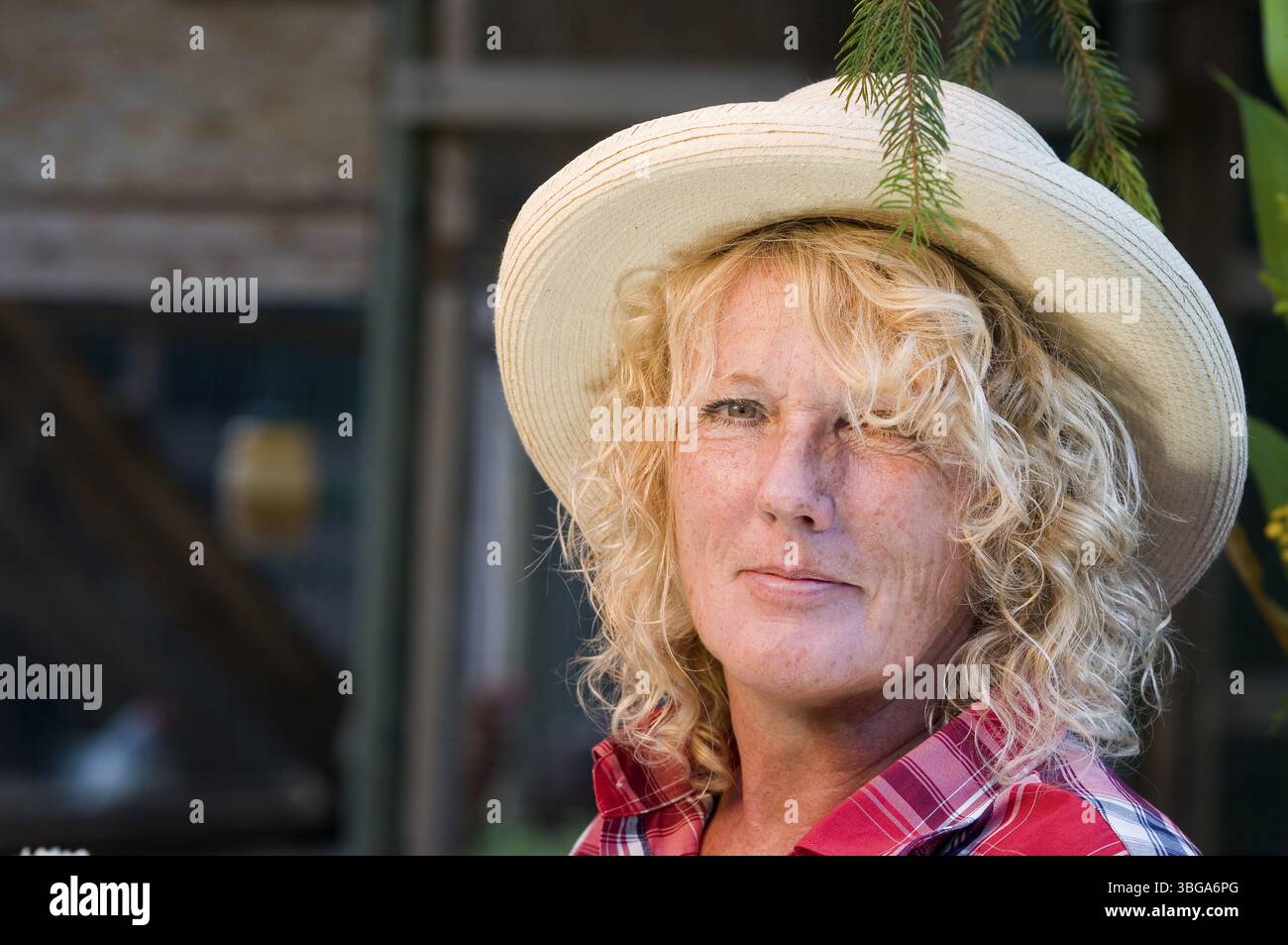 Ritratto laterale della testa all'aperto di una donna di mezza età con cappello di paglia che sorride nella fotocamera Foto Stock
