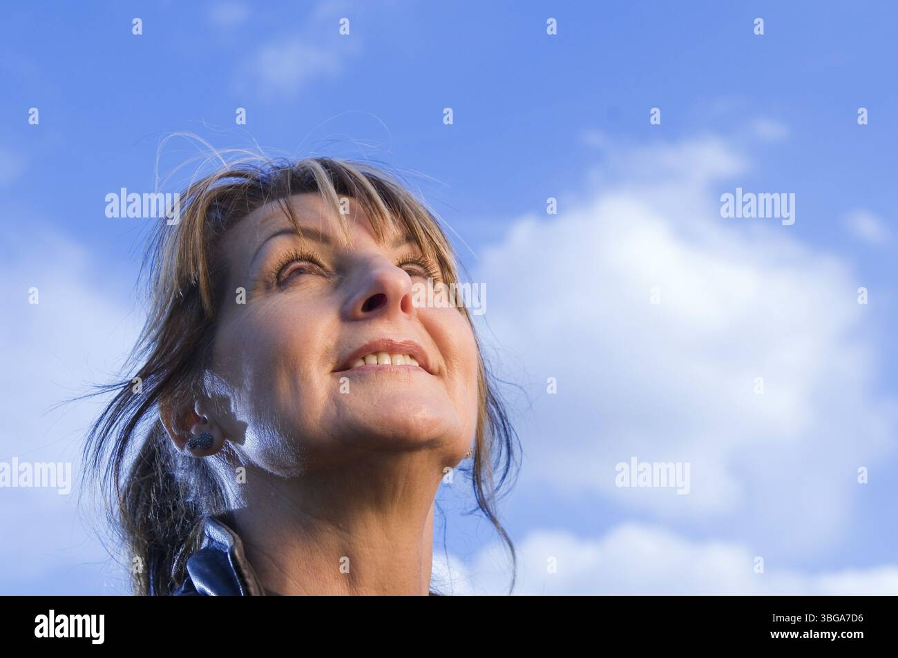Ritratto della testa di una donna di mezza età che sorride felicemente verso l'alto nel cielo blu Foto Stock