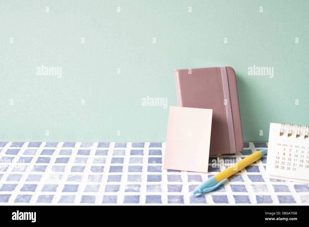 Diario, penna e calendario sulla scrivania con piastrelle blu. sfondo muro menta. area di lavoro Foto Stock