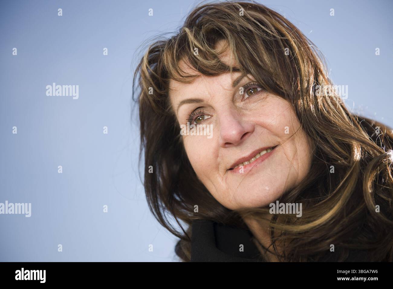 Ritratto della testa di una donna di mezza età che guarda con gioia di lato davanti a un cielo blu Foto Stock