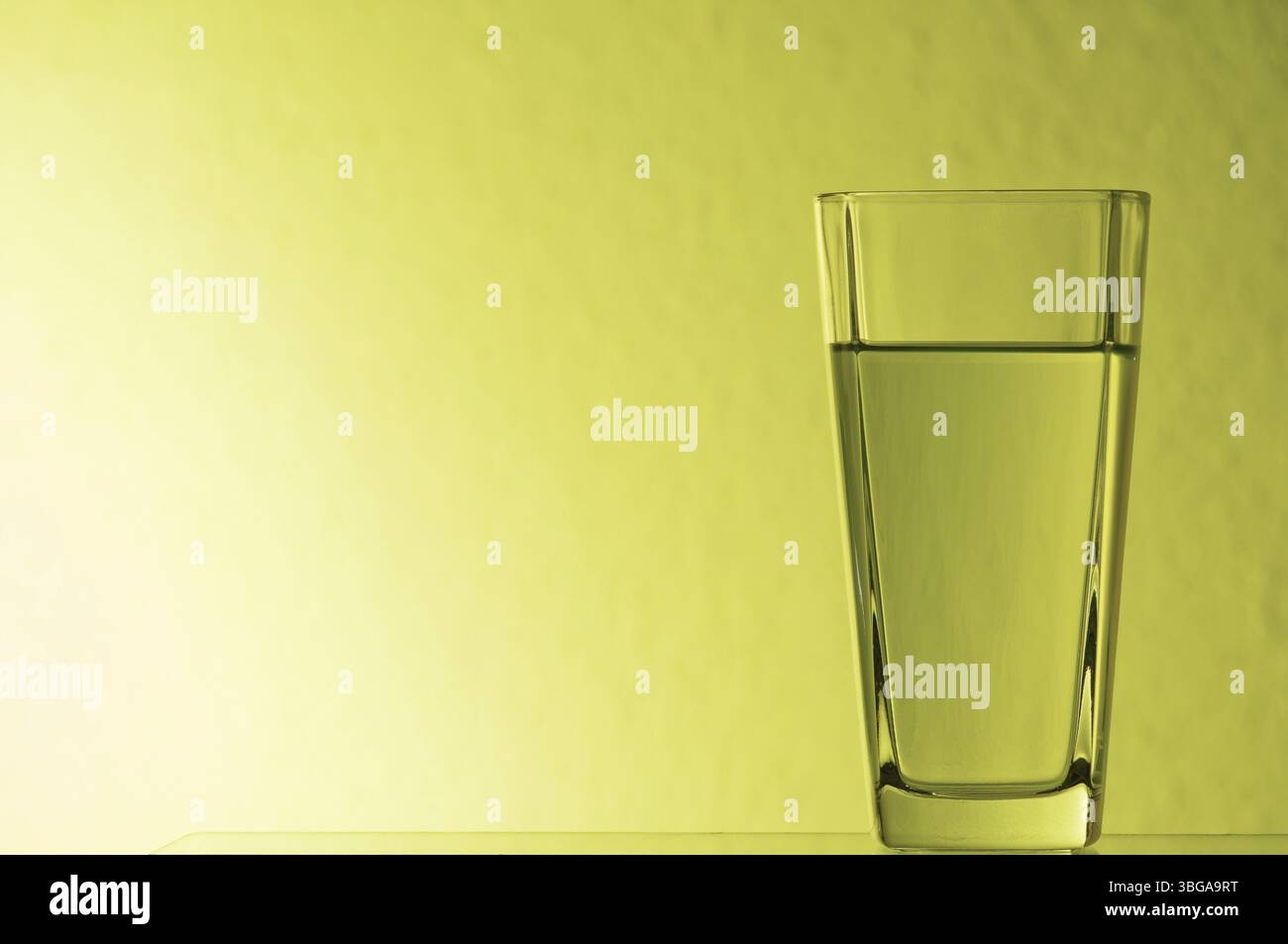 Natura morta con vetro limonato su lastra di vetro illuminata in giallo Foto Stock