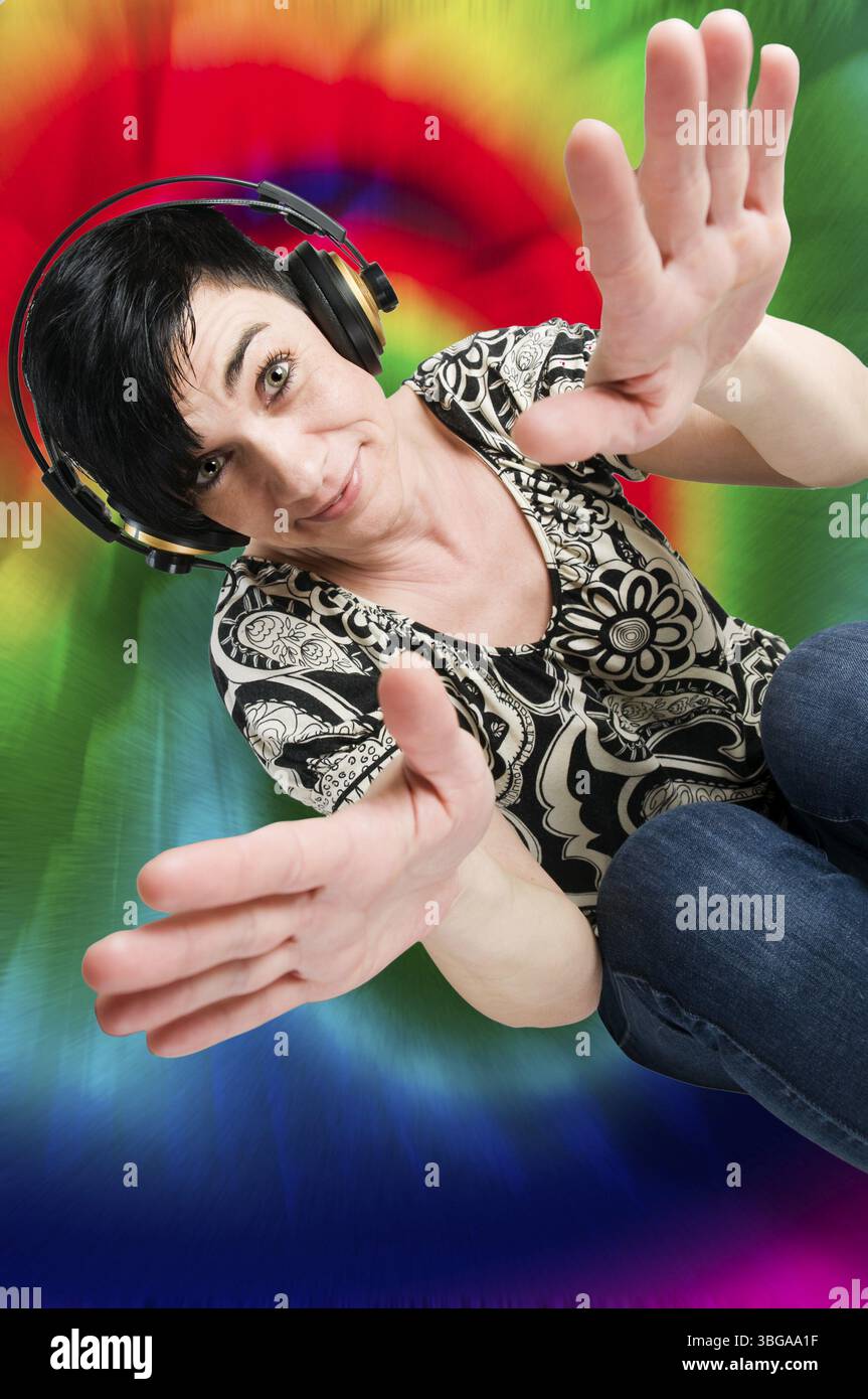 Vista della parte superiore del corpo di una donna di mezza età dai capelli neri con cuffie davanti a uno sfondo colorato Foto Stock