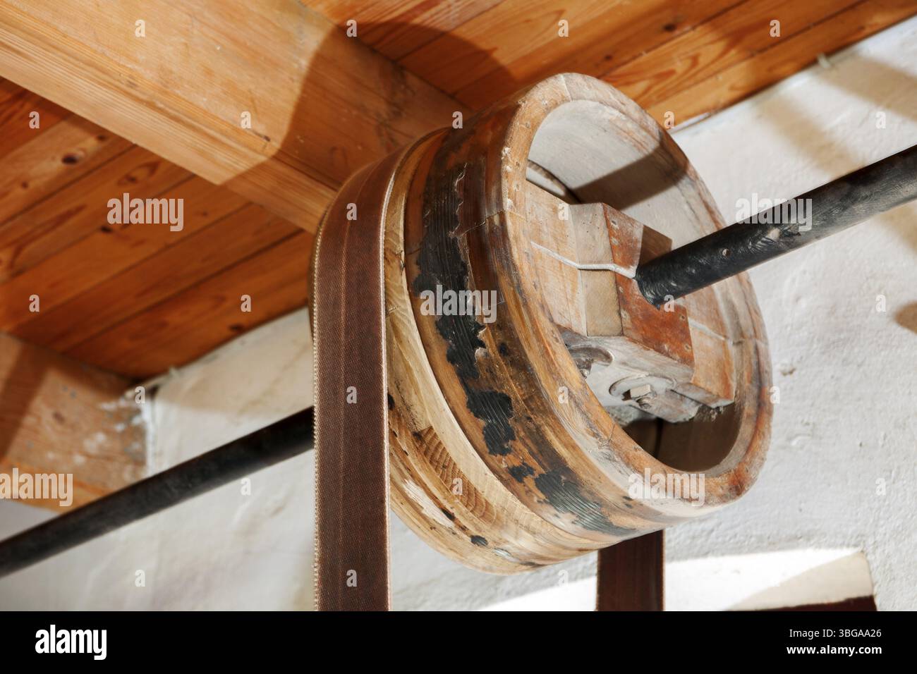 Vecchia ruota di legno su un albero come parte di una trasmissione sotto le travi del soffitto di una vecchia fabbrica di falegname Foto Stock