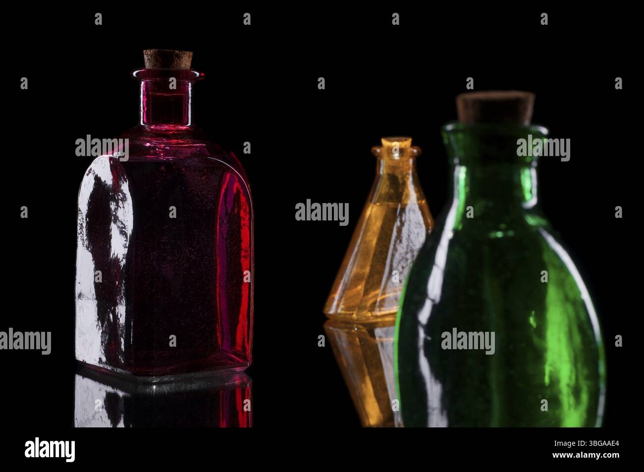 STILL Life di tre bottiglie decorative colorate con tappi in sughero su vetro su sfondo nero Foto Stock
