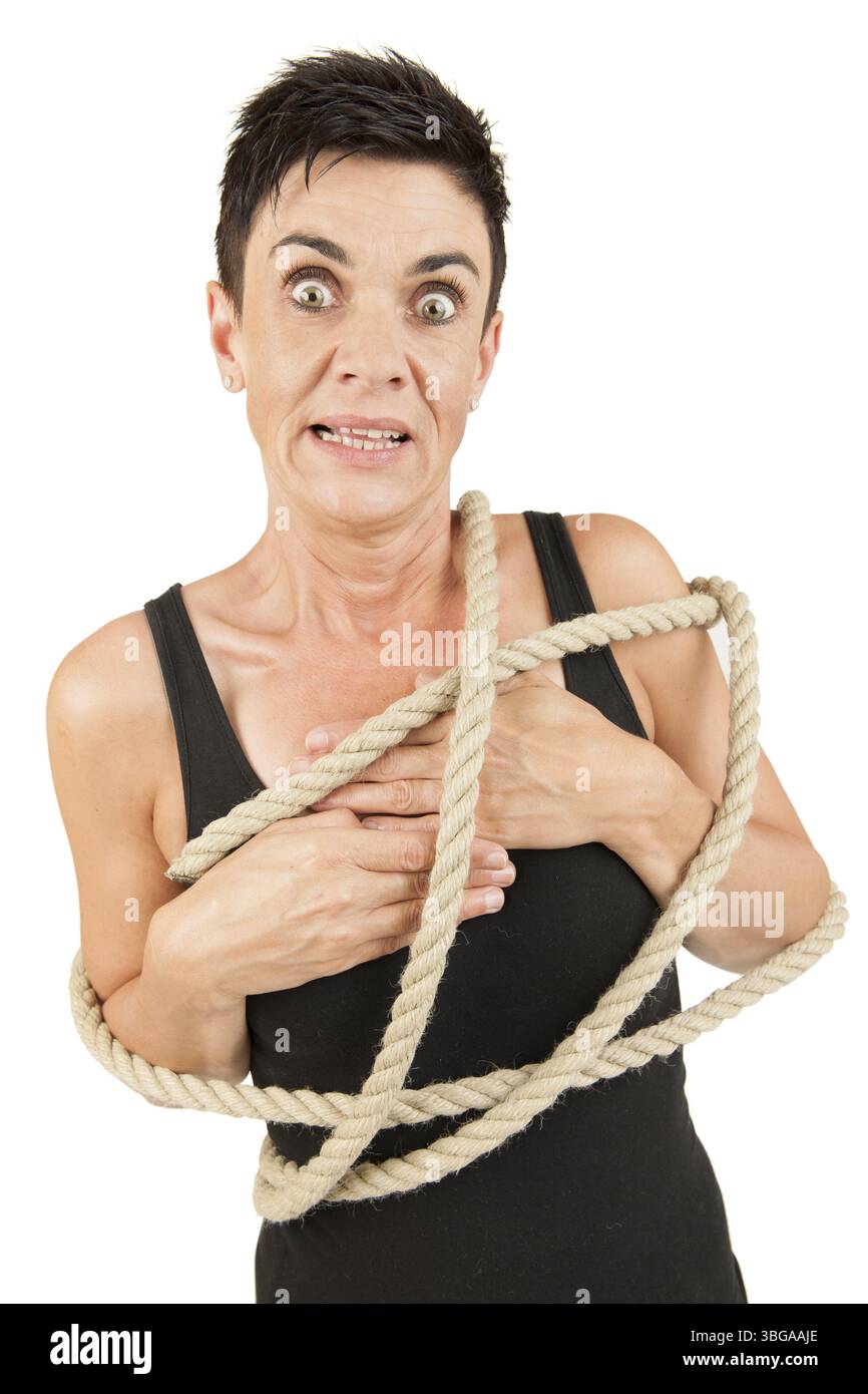 Vista frontale della parte superiore del corpo di una donna di mezza età dai capelli neri con una corda intorno al corpo che sembra scossa nella telecamera di fronte a una W. Foto Stock