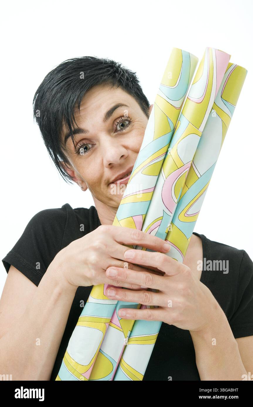 Vista della testa e delle spalle di una donna di mezza età dai capelli neri che tiene davanti a sé rotoli di carta da imballaggio giallo-verde su sfondo bianco Foto Stock