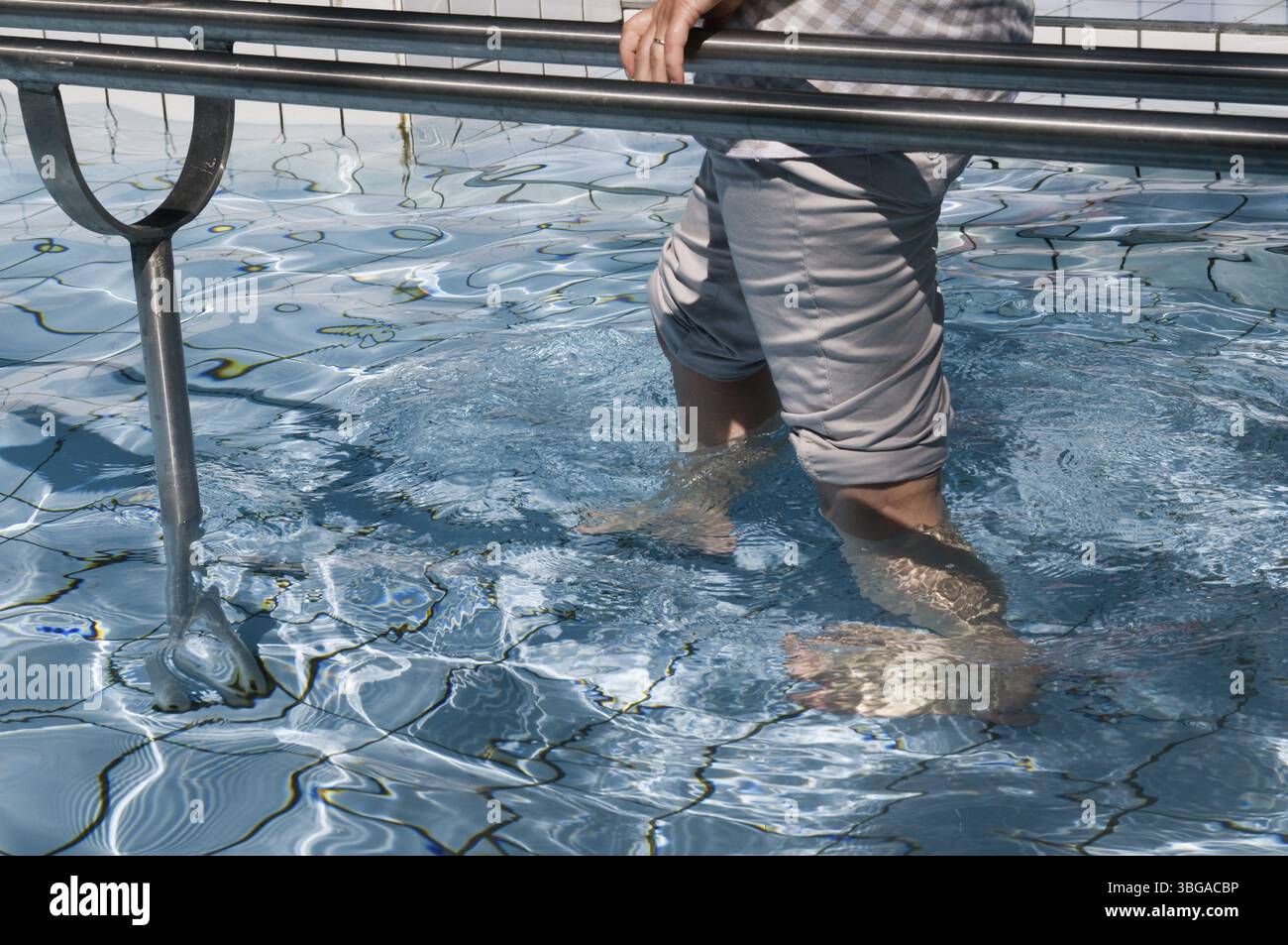 Foto esterna di gambe femminili che camminano in acqua (cura Kneipp) in una piscina piastrellata con corrimano in acciaio inox Foto Stock