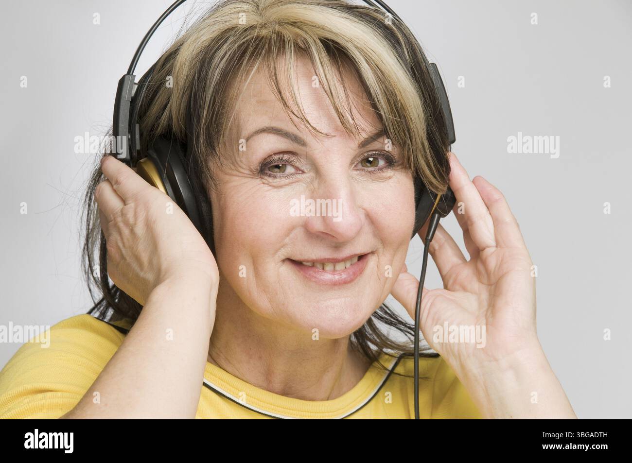 Foto testa e spalle di una donna di mezza età con cuffie che ascoltano musica e suoni su uno sfondo bianco Foto Stock