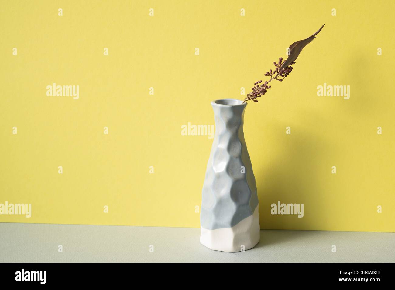 Vaso in ceramica blu con fiore secco su ripiano grigio. sfondo giallo della parete. Design interno minimalista Foto Stock