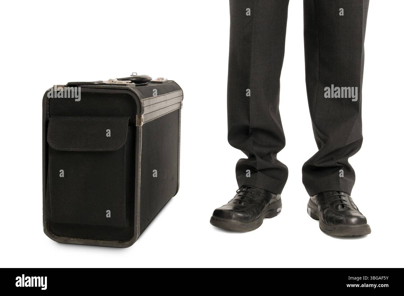 Gambe maschili con pantaloni e scarpe nere e valigetta in piedi accanto ad essa con ombra su sfondo bianco.wgambe maschili con pantaloni e bla neri Foto Stock