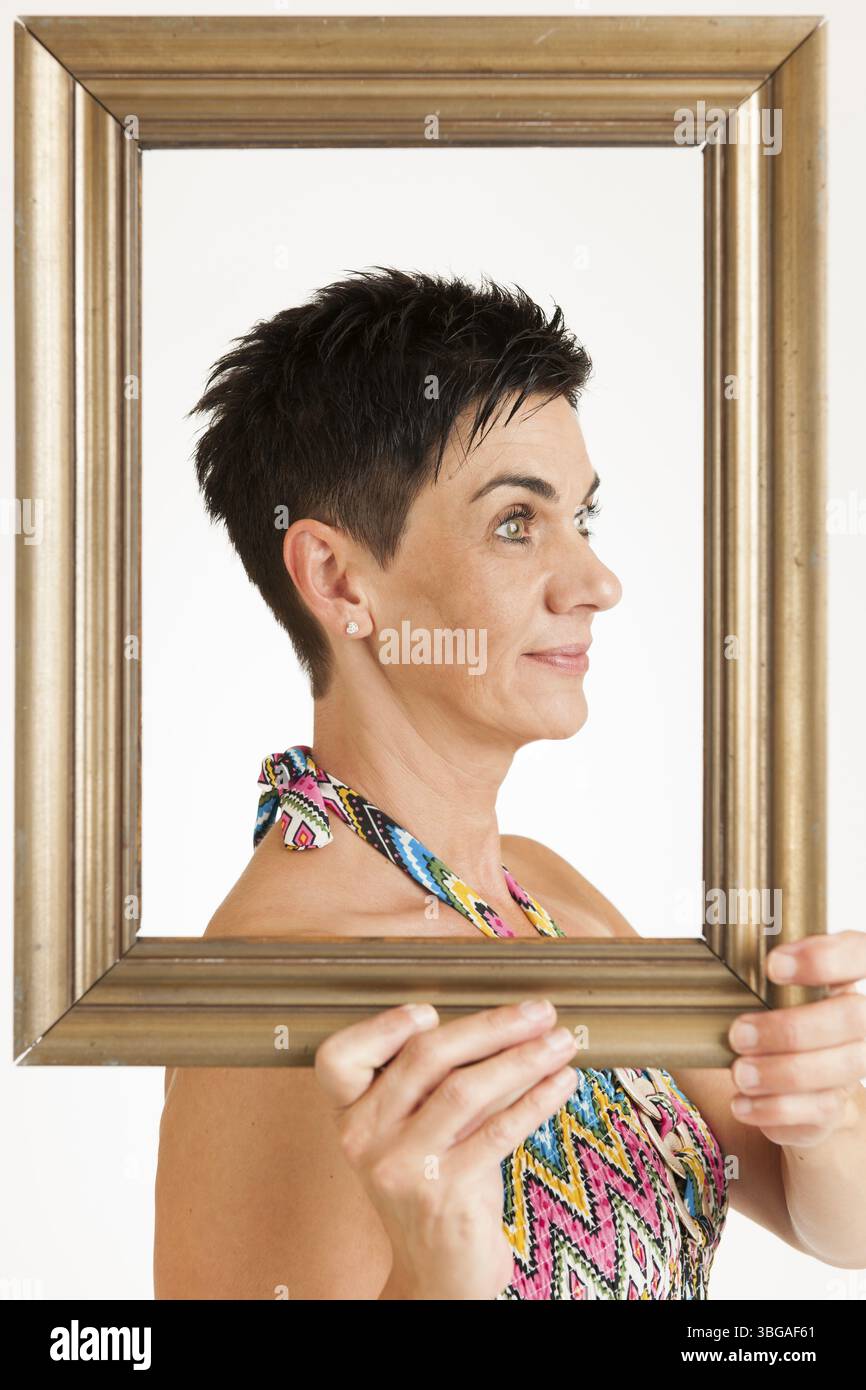 Vista della parte superiore del corpo di una donna di mezza età dai capelli neri con cornice dorata su sfondo bianco, Berlino, Germania, Europa Foto Stock