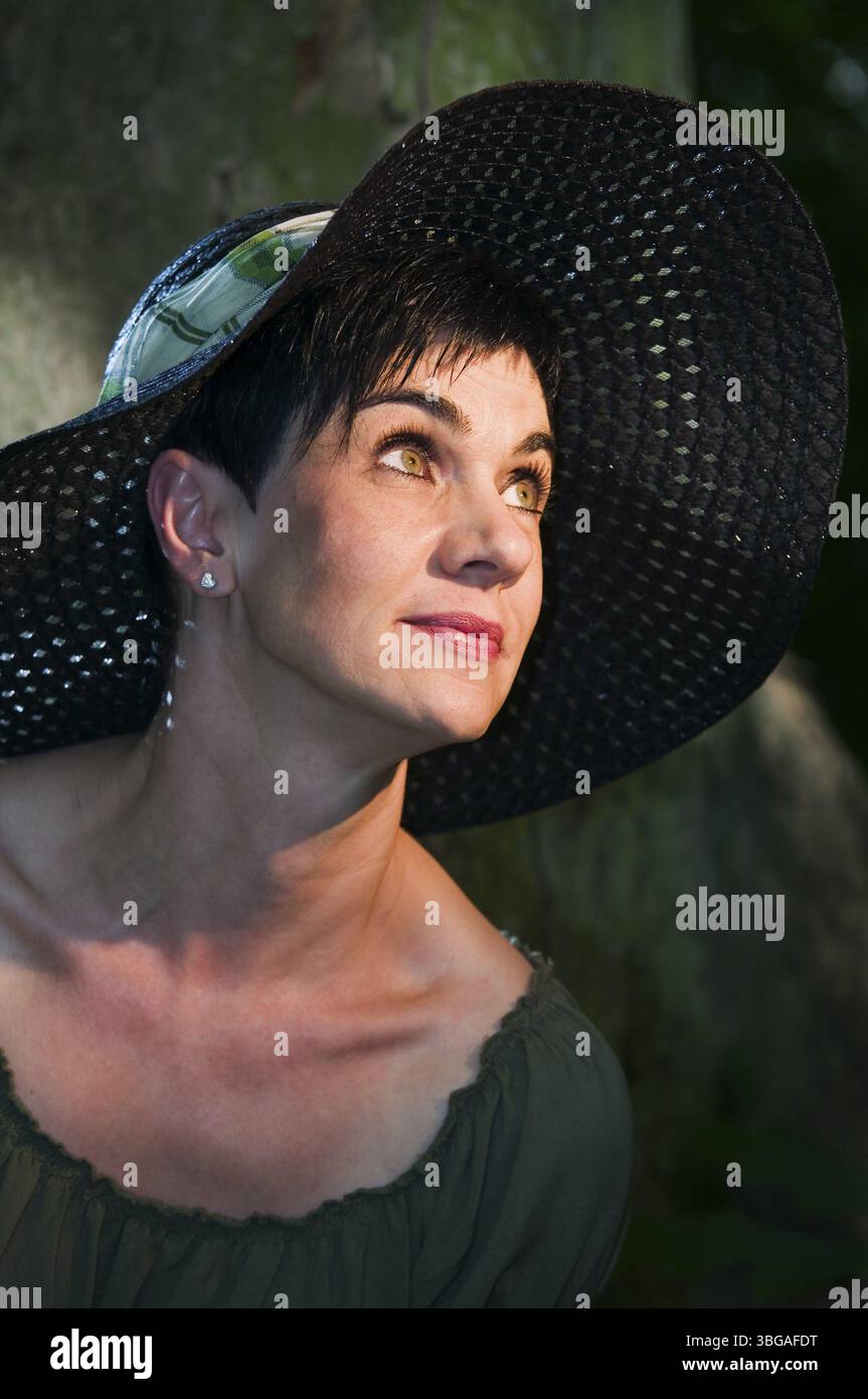 Vista laterale della testa e delle spalle di una donna dai capelli neri di mezza età con un cappello da sole nero nero rivolto verso l'alto da un lato Foto Stock