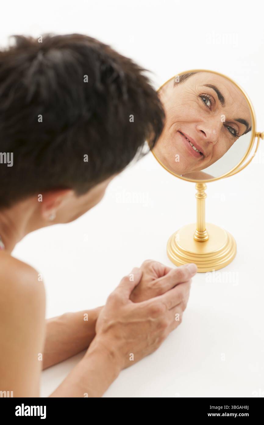 Volto di una donna di mezza età in uno specchio rotondo per il trucco su sfondo bianco Foto Stock