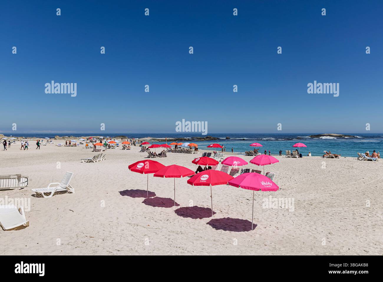 Ombrelloni rossi sulla spiaggia soleggiata di Camps Bay, un sobborgo di città del Capo sulla costa occidentale della Penisola del Capo Foto Stock