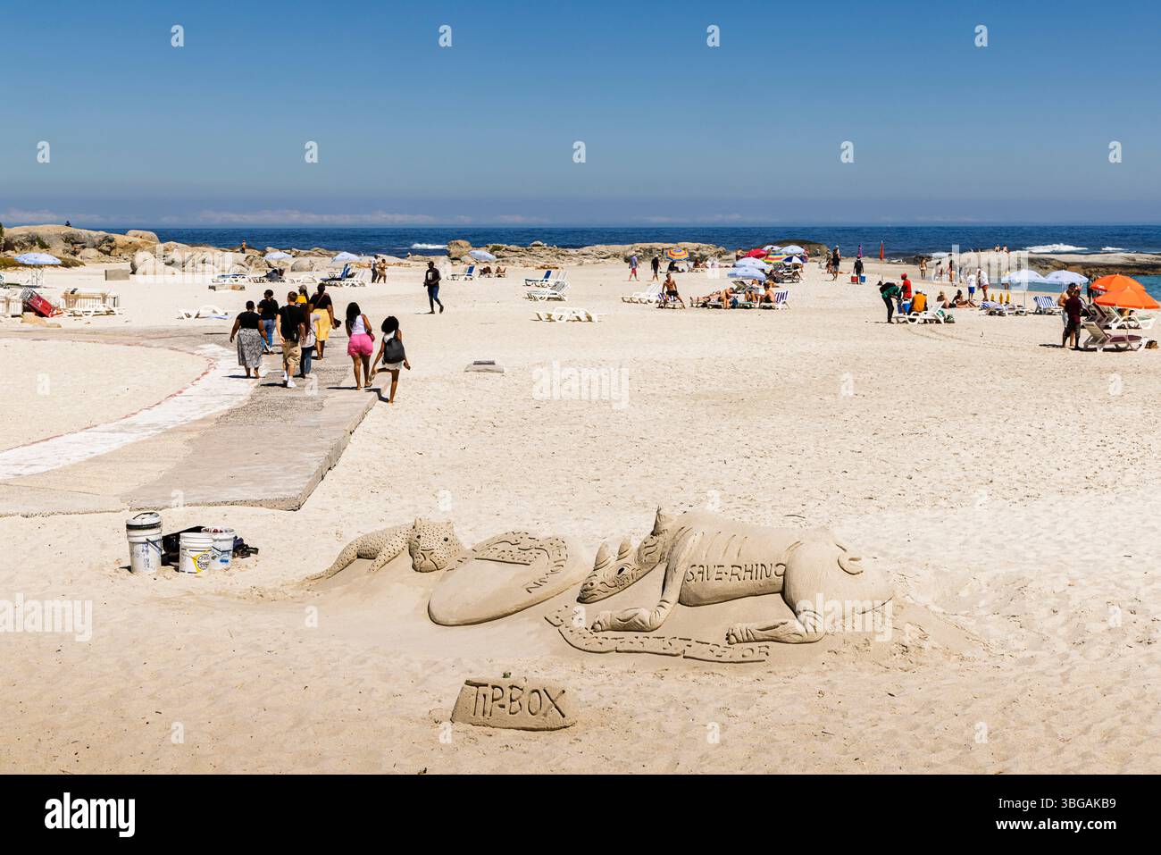 La spiaggia di Camps Bay, un sobborgo di città del Capo sulla costa occidentale della Penisola del Capo con una scultura di sabbia Save the Rhino per suggerimenti Foto Stock
