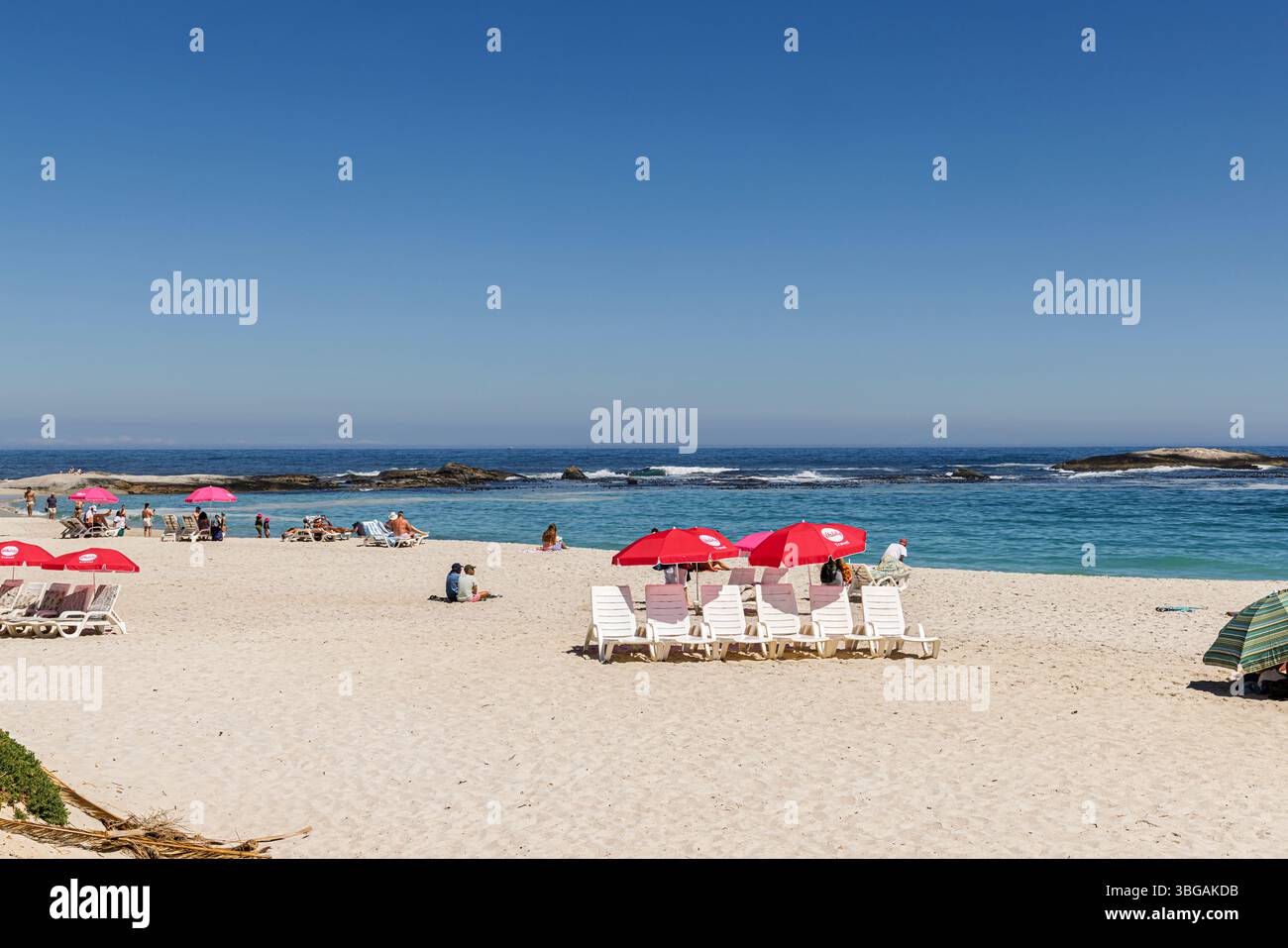 Ombrelloni rossi sulla spiaggia soleggiata di Camps Bay, un sobborgo di città del Capo sulla costa occidentale della Penisola del Capo Foto Stock