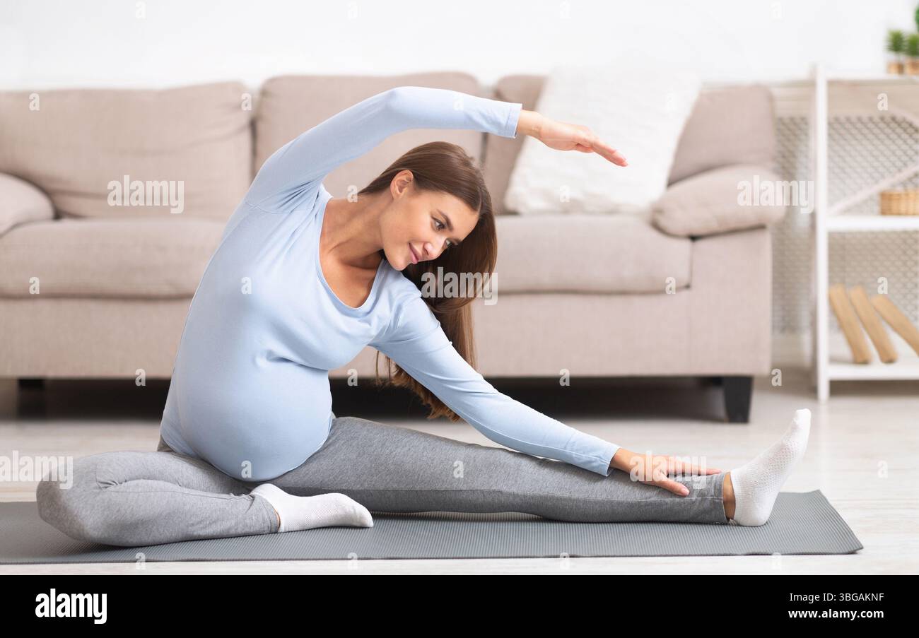 Calma la donna incinta facendo esercizi di stretching a casa Foto Stock